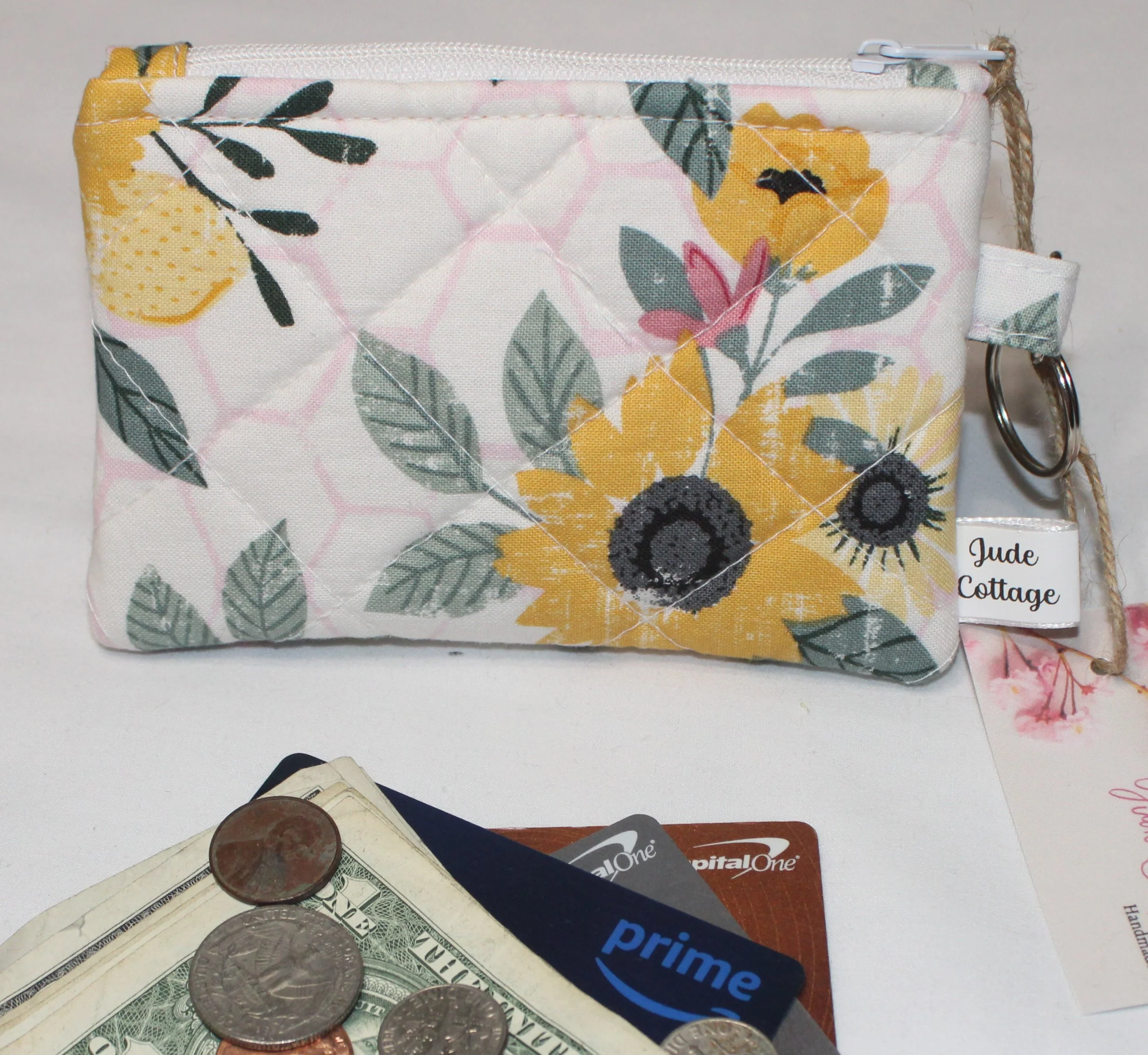 Front view of the Honeycomb Sunflower quilted wallet with a sunflower and floral print, zipper top, and an attached keyring, shown with cash, cards, and coins to illustrate use.