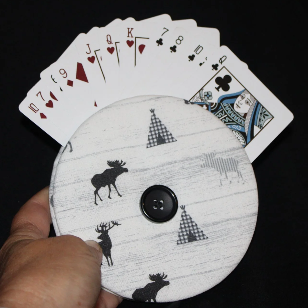 Front view of the Moose Camp Card Holder featuring moose, deer, and teepee motifs on white fabric shown in use being held with an array of playing cards.