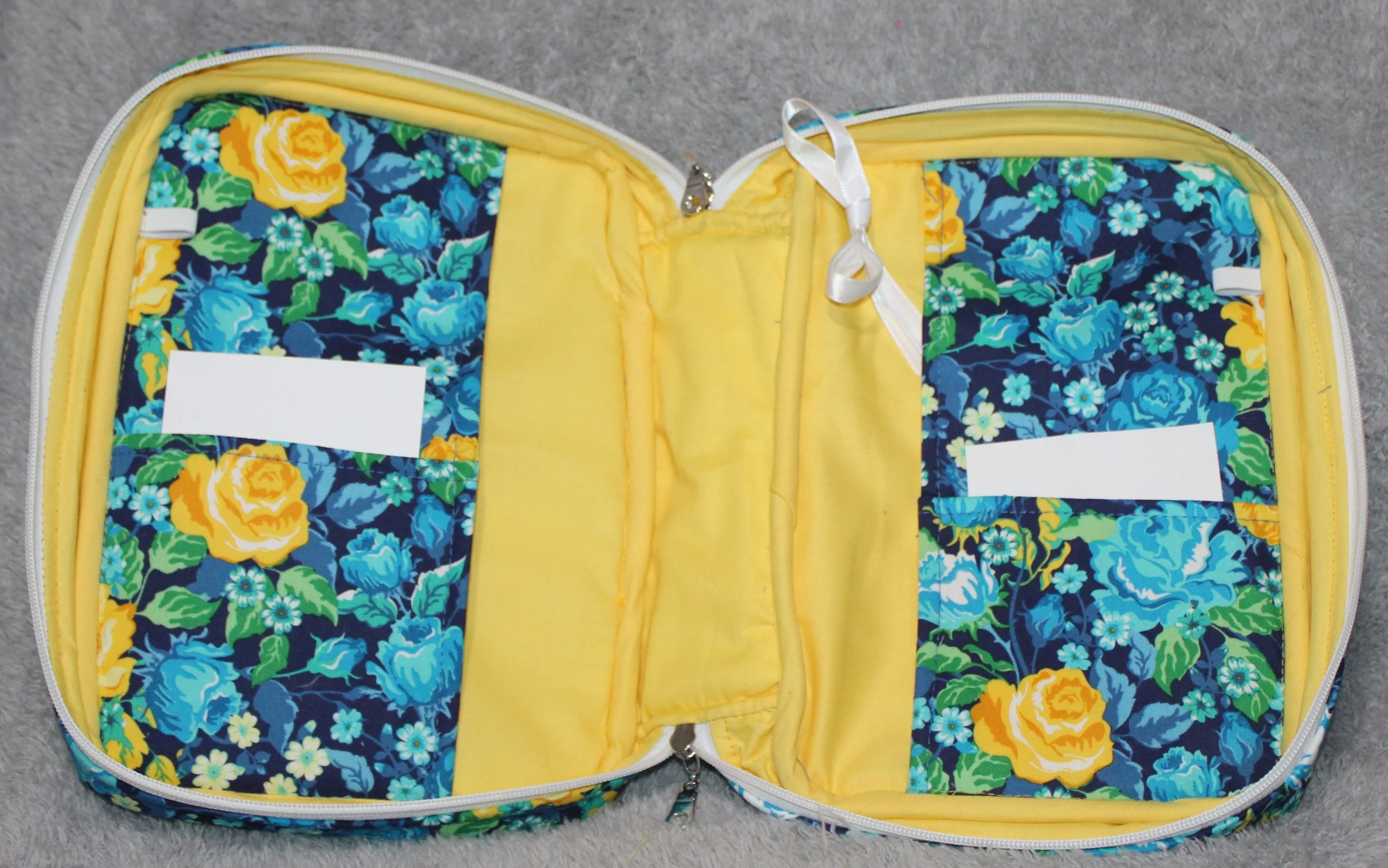 Empty interior view of the Raisa Bible study case showing slip pockets, pen holders, ribbons, and the yellow lining with blue floral panels.