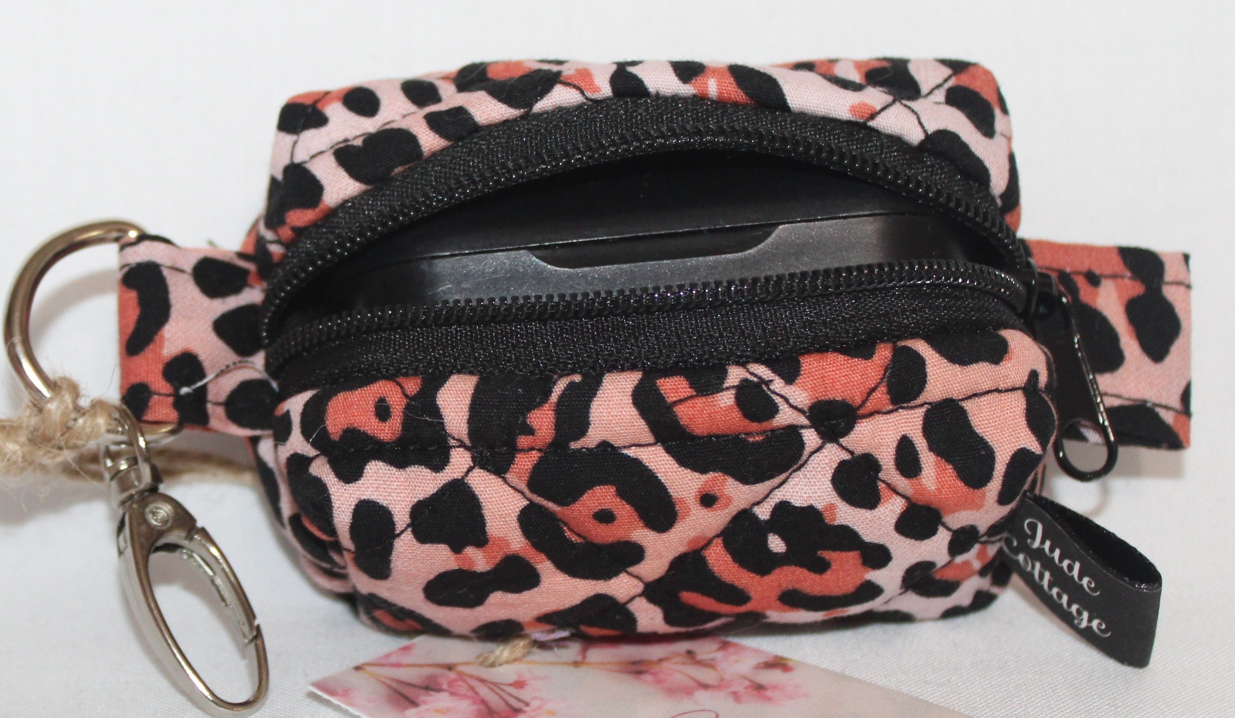 Top open view of the Mia Bag Charm featuring pink leopard print fabric shown with a set of J Lab earbuds inserted for sizing reference..