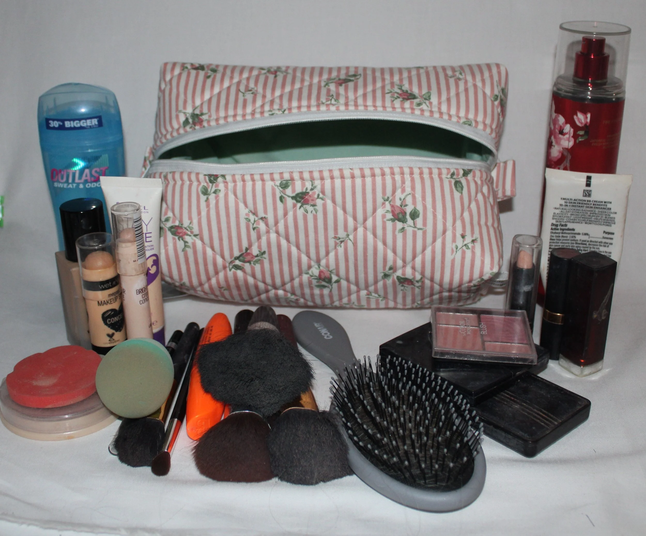 Top angled view of the large Victoria quilted travel pouch in pink floral stripe print displayed with cosmetics arranged around it to show size.