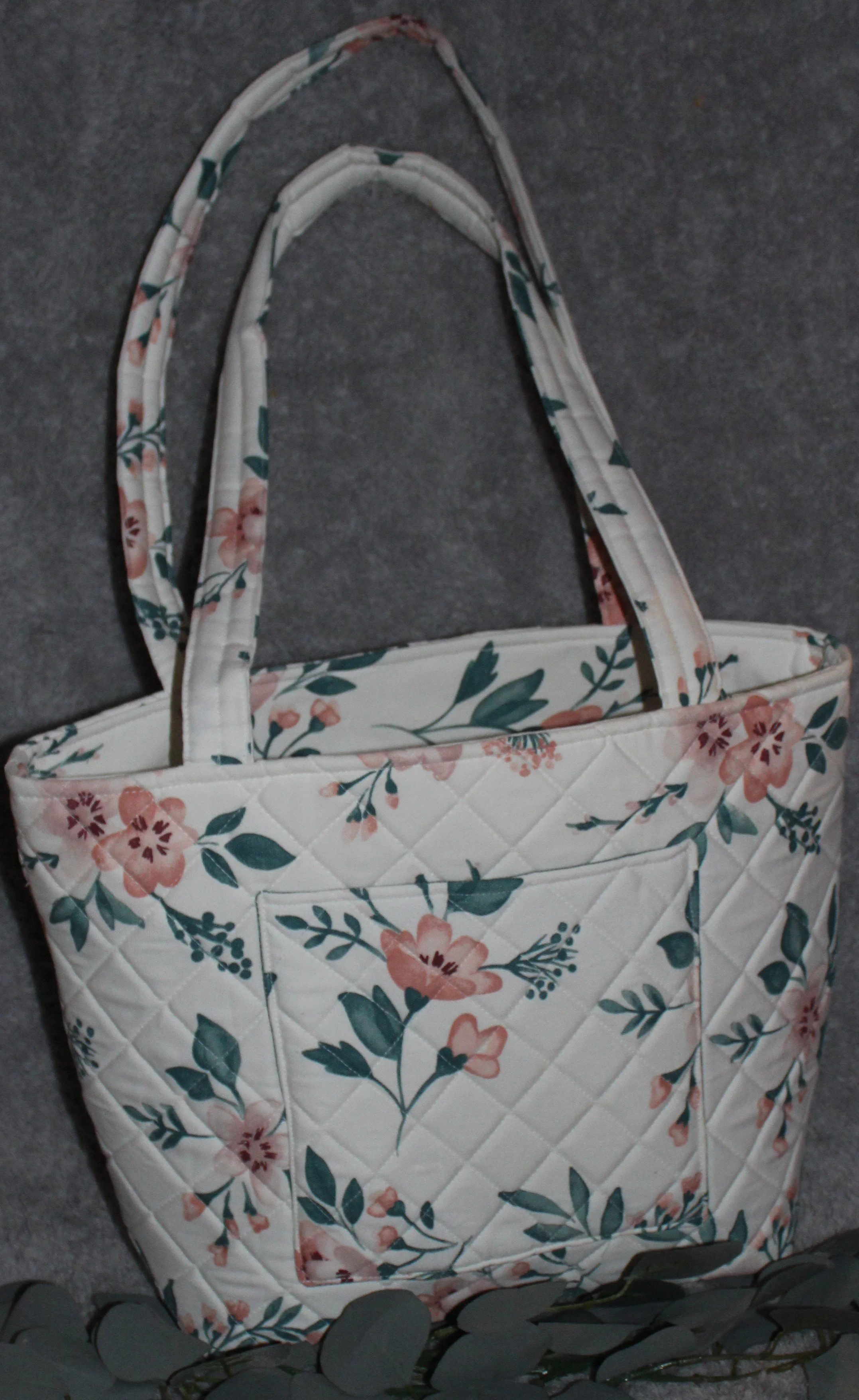 Back view of the Odette quilted tote in white fabric with a pink floral pattern, showing the quilted exterior, two padded shoulder straps, and one exterior slip pocket.