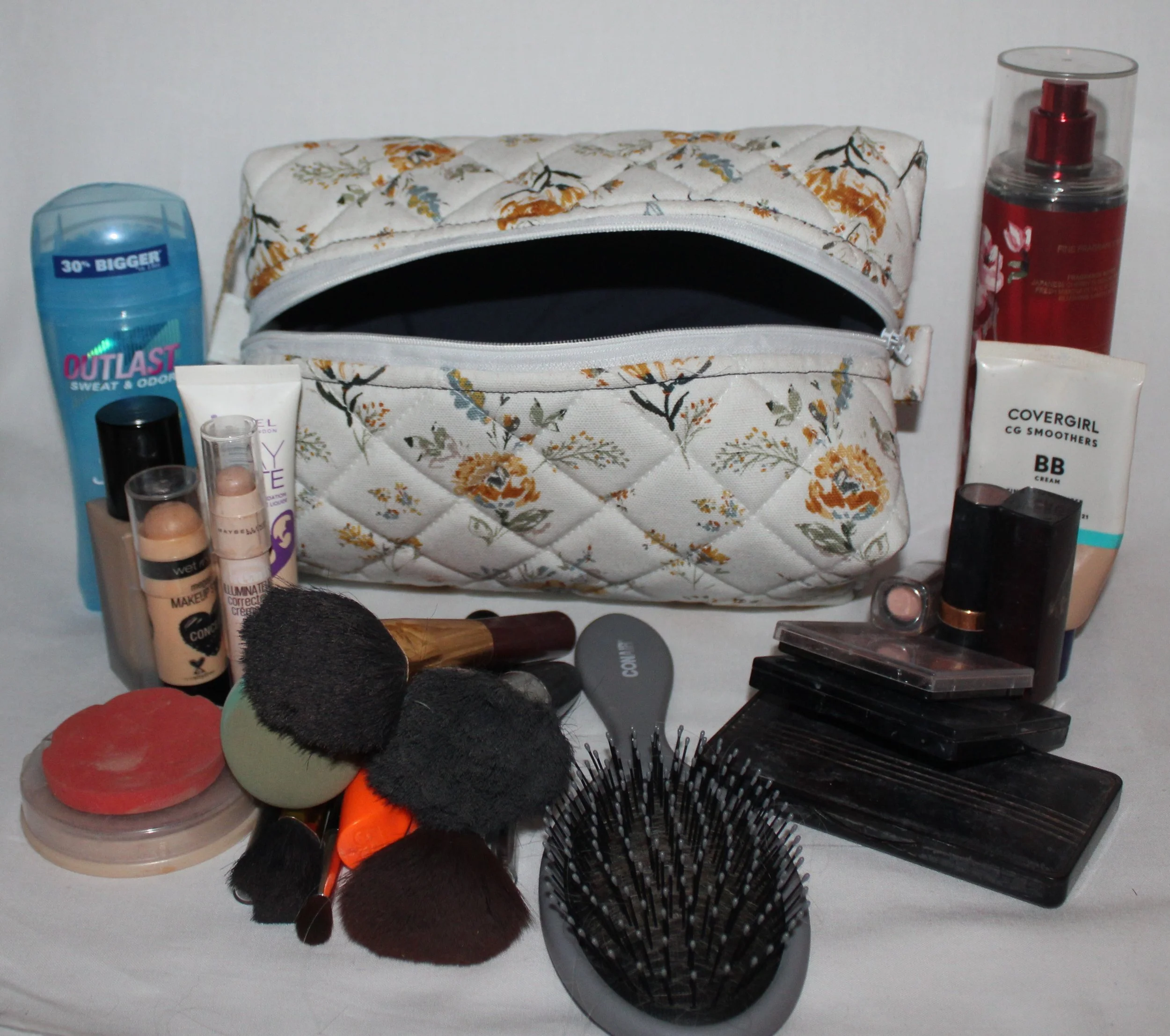 Large Dandelion Blue quilted floral travel pouch displayed with makeup and personal care items arranged around it for scale.