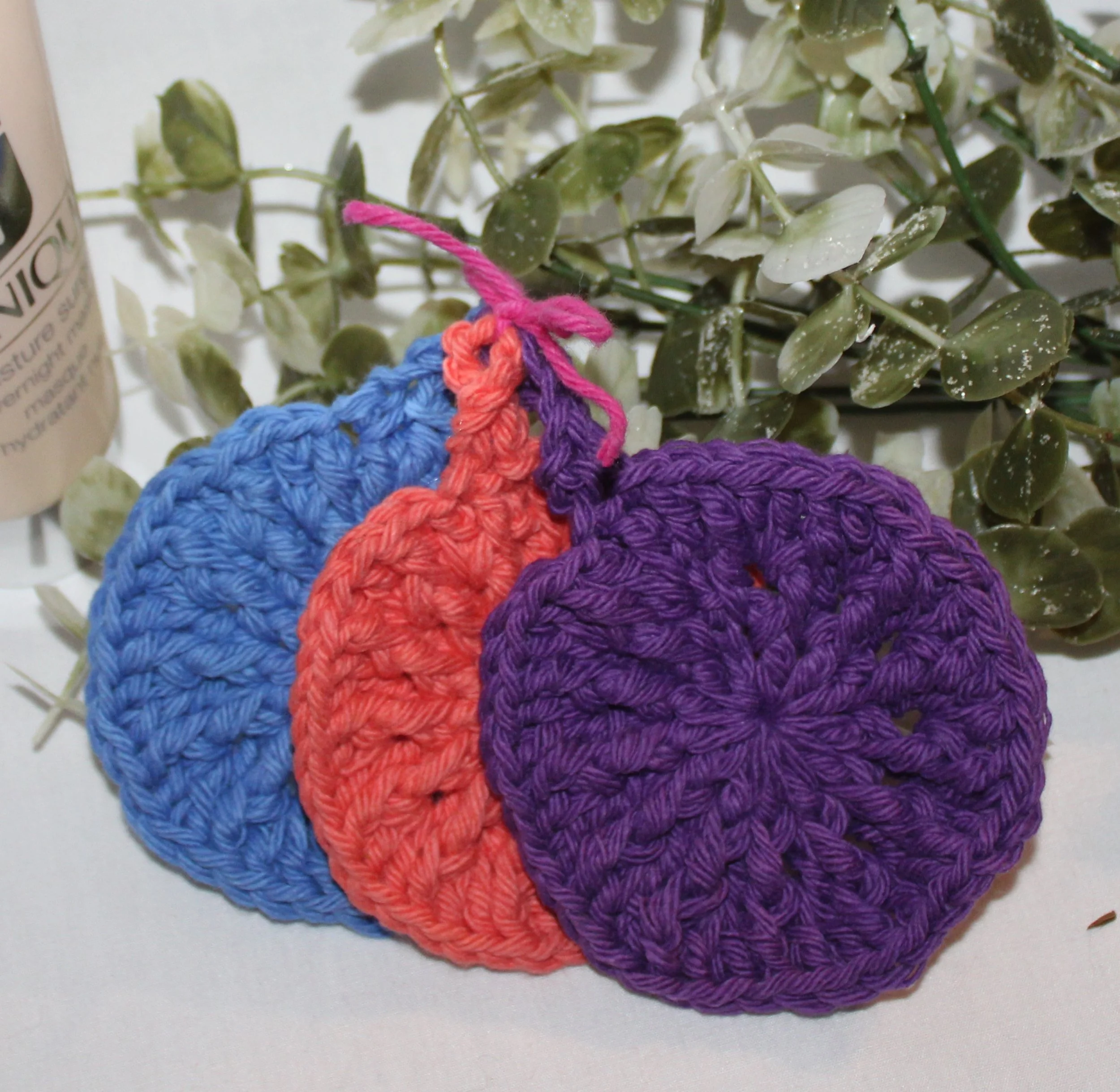 Close‑up of round crocheted assorted colors of blue coral plum facial scrubbies with a textured stitch pattern.