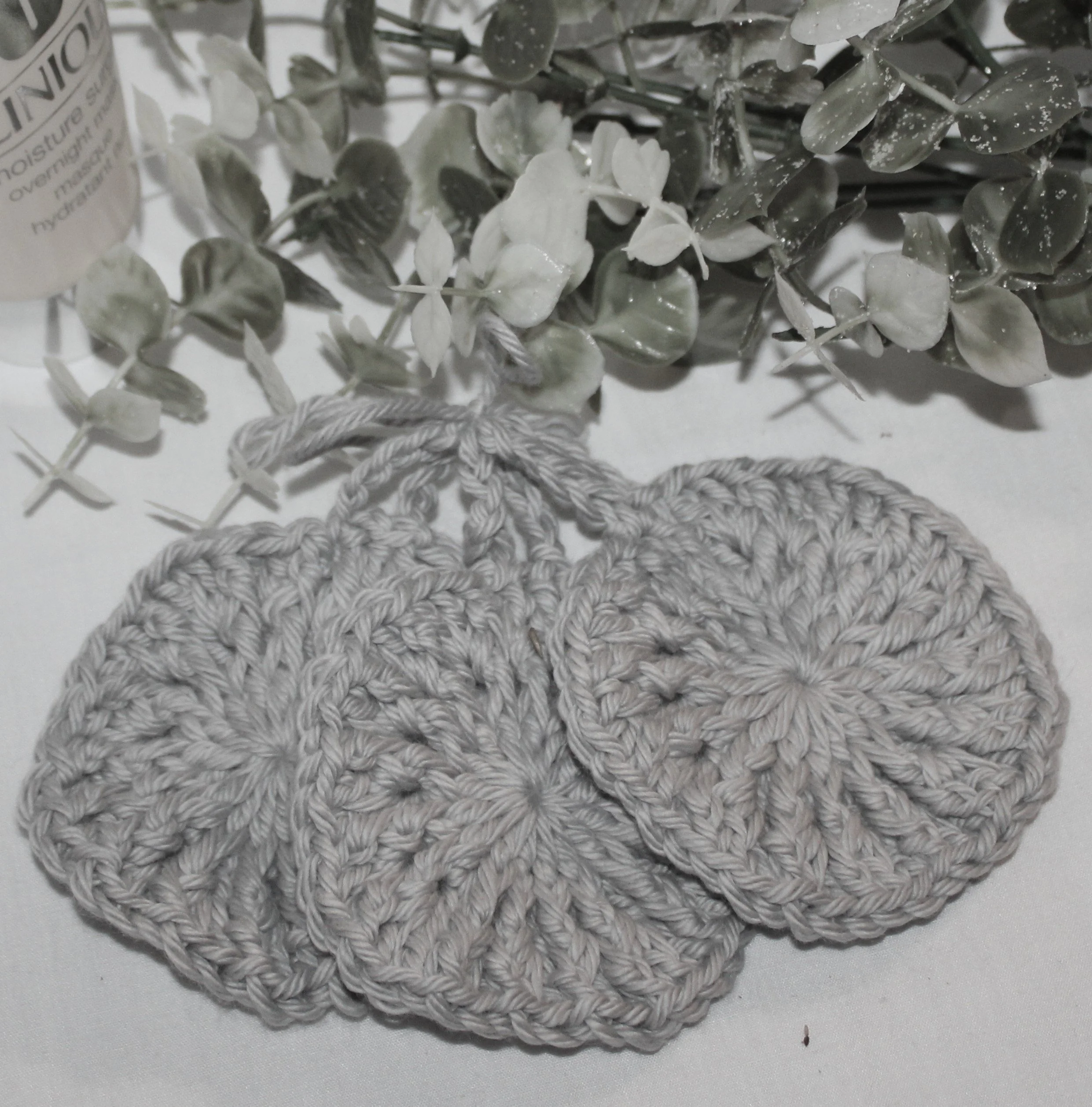 Close‑up of round crocheted silver facial scrubbies with a textured stitch pattern.