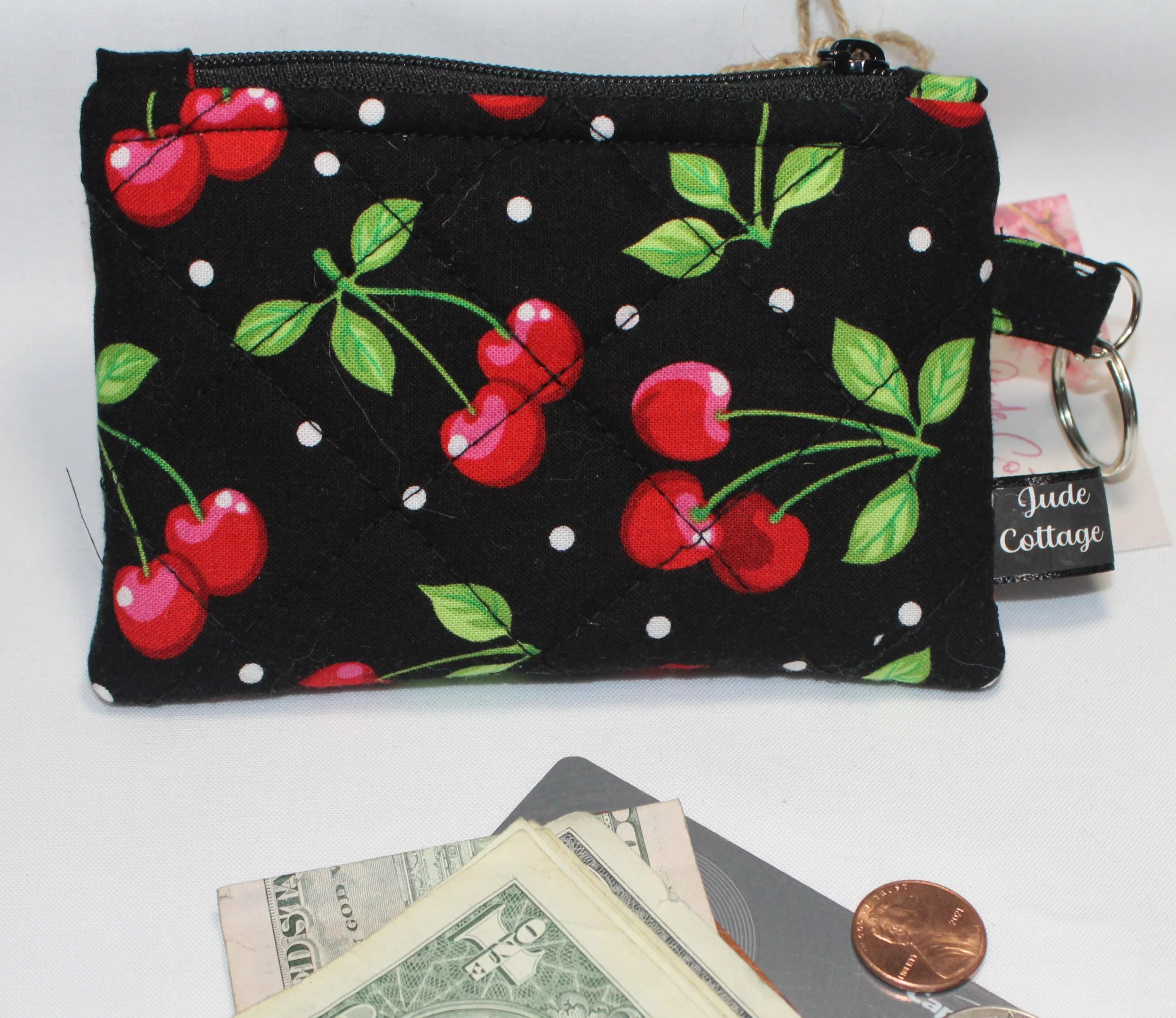 Quilted keychain wallet with scattered red cherries on dark fabric, zipper closure, and metal key ring.