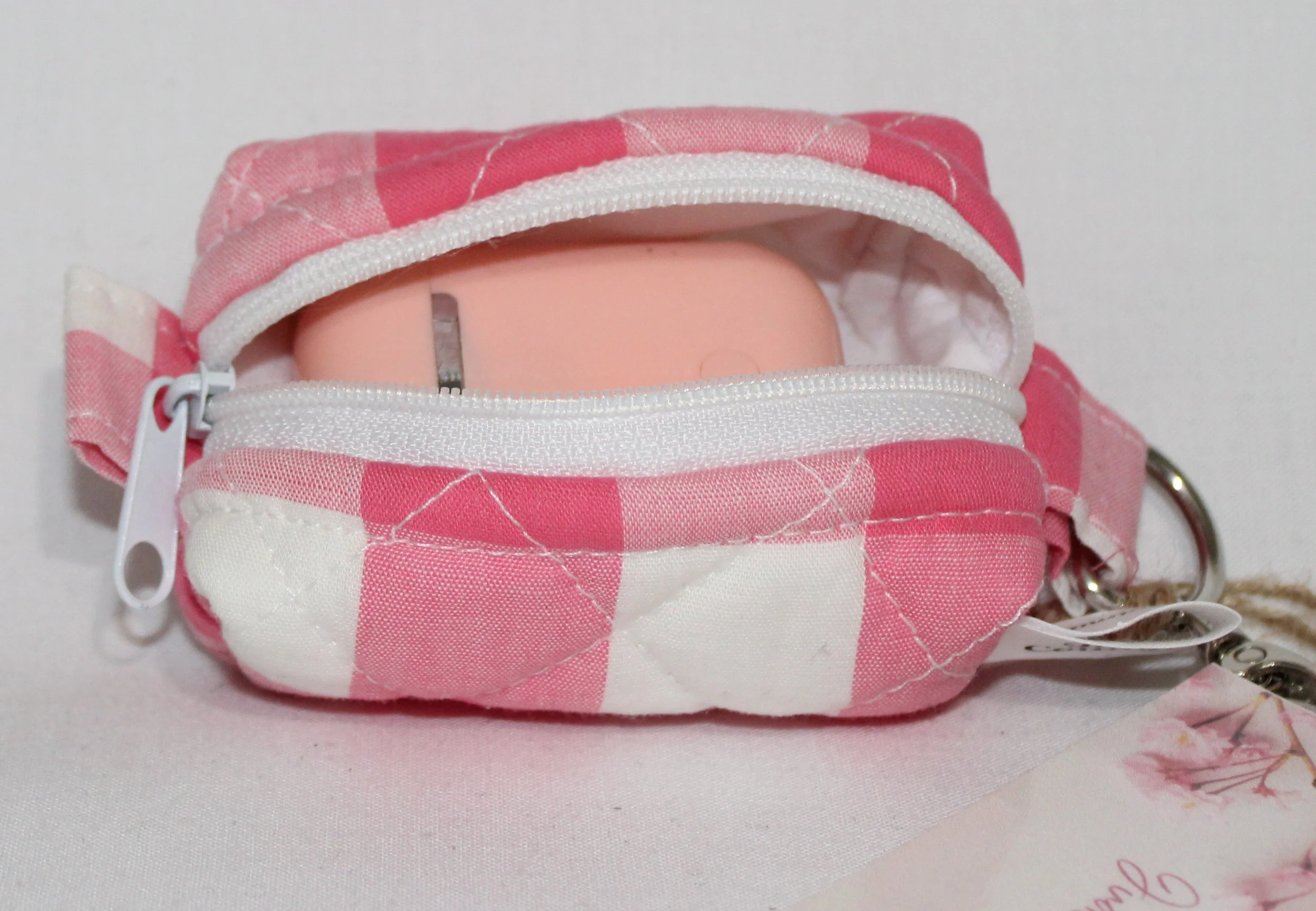 Top open view of the Sophie Bag Charm featuring a pink and white check fabric shown with an Airpod earbud case inserted to demonstrate sizing.