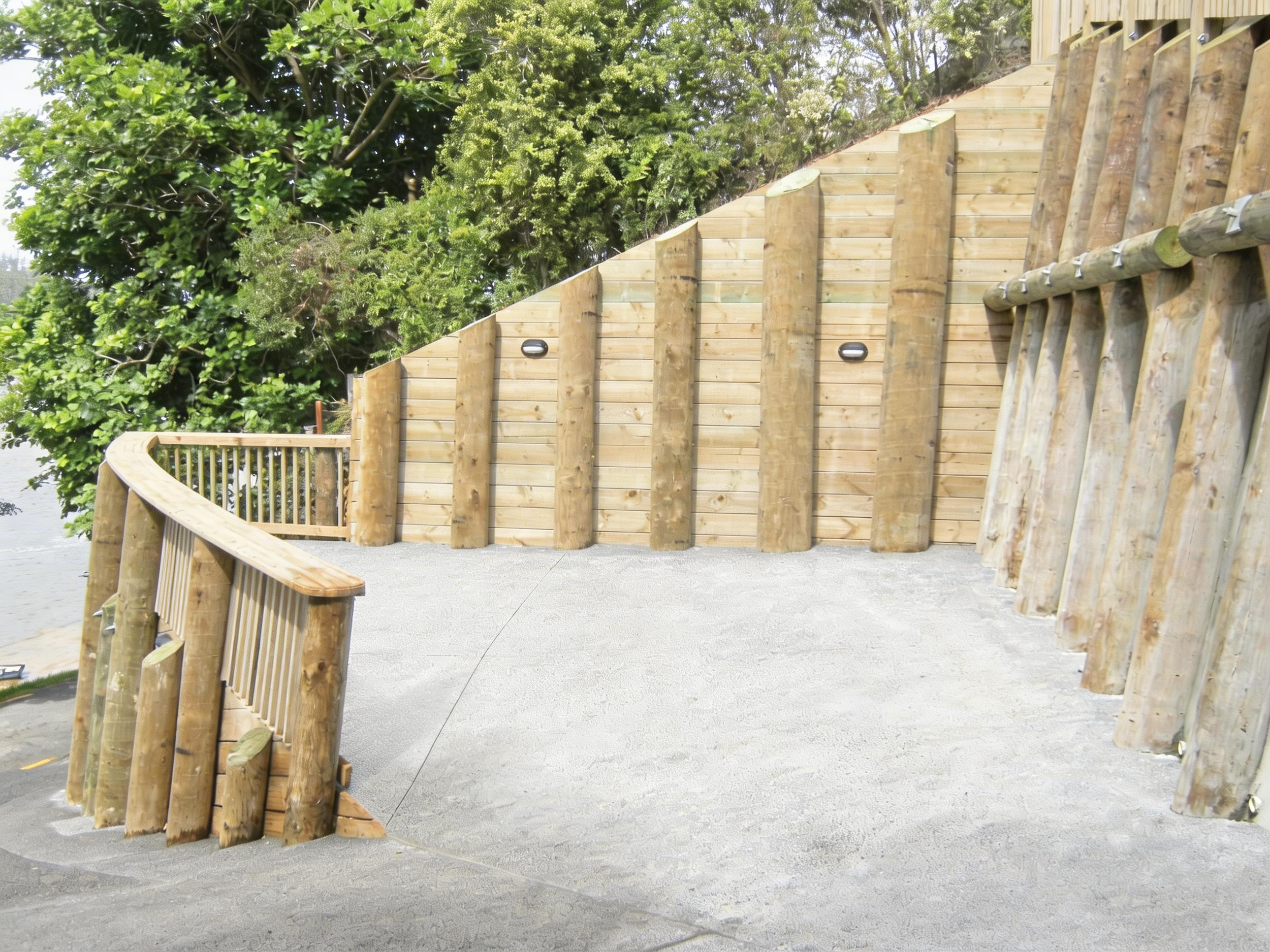 A wooden outdoor deck with a curved railing, wooden fence, and lush green trees in the background.