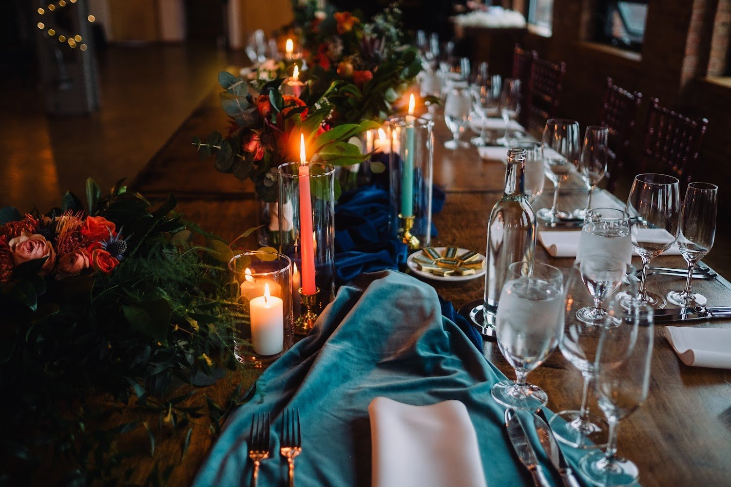 A beautifully decorated dinner table with lit candles, flowers, wine glasses, water glasses, and napkins for an elegant event or celebration.