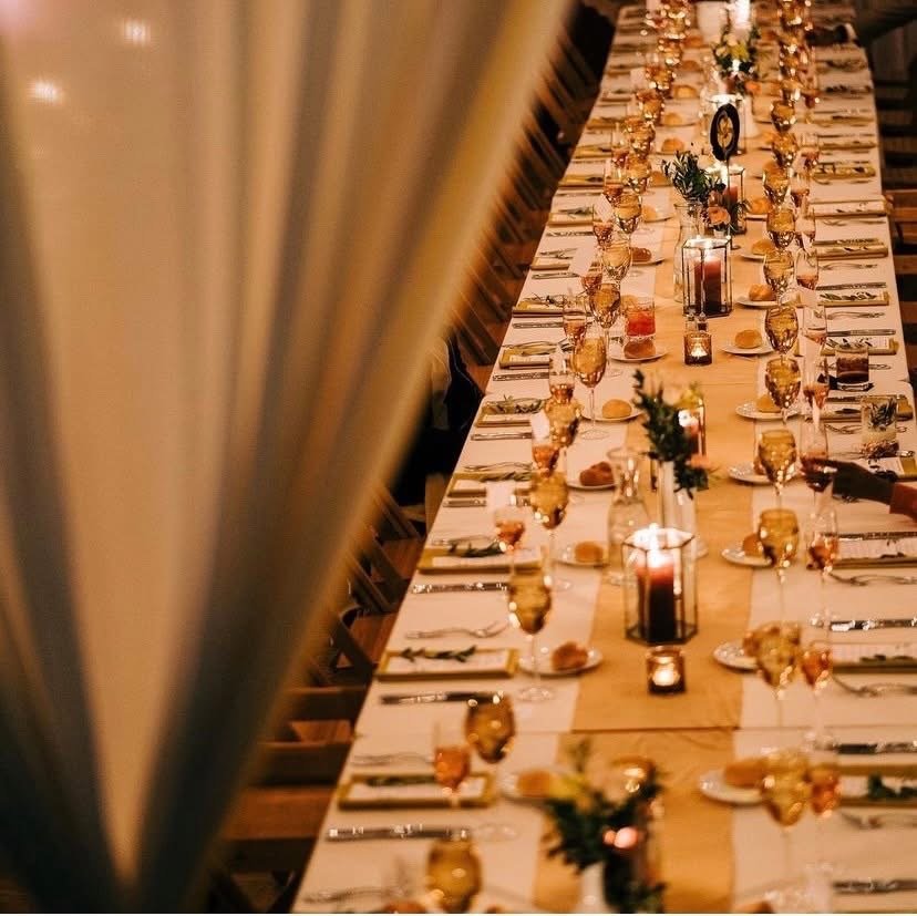 Long dining table set for a celebration with candles, glasses, plates, and floral centerpieces.