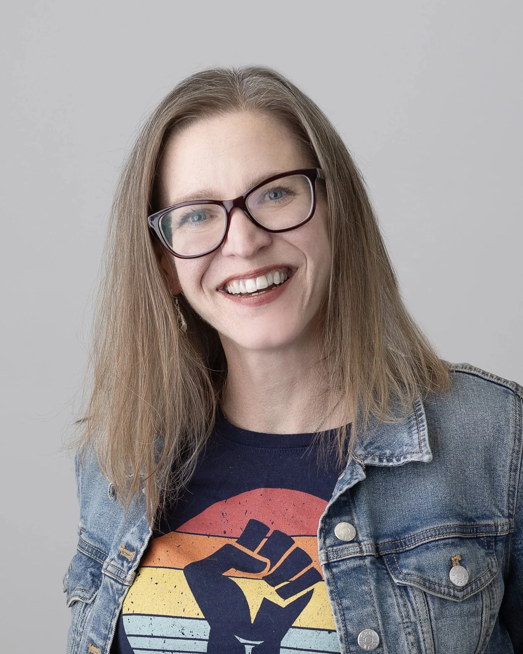Erin McCrossan in a colorful RESIST tshirt, jean jacket, and glasses