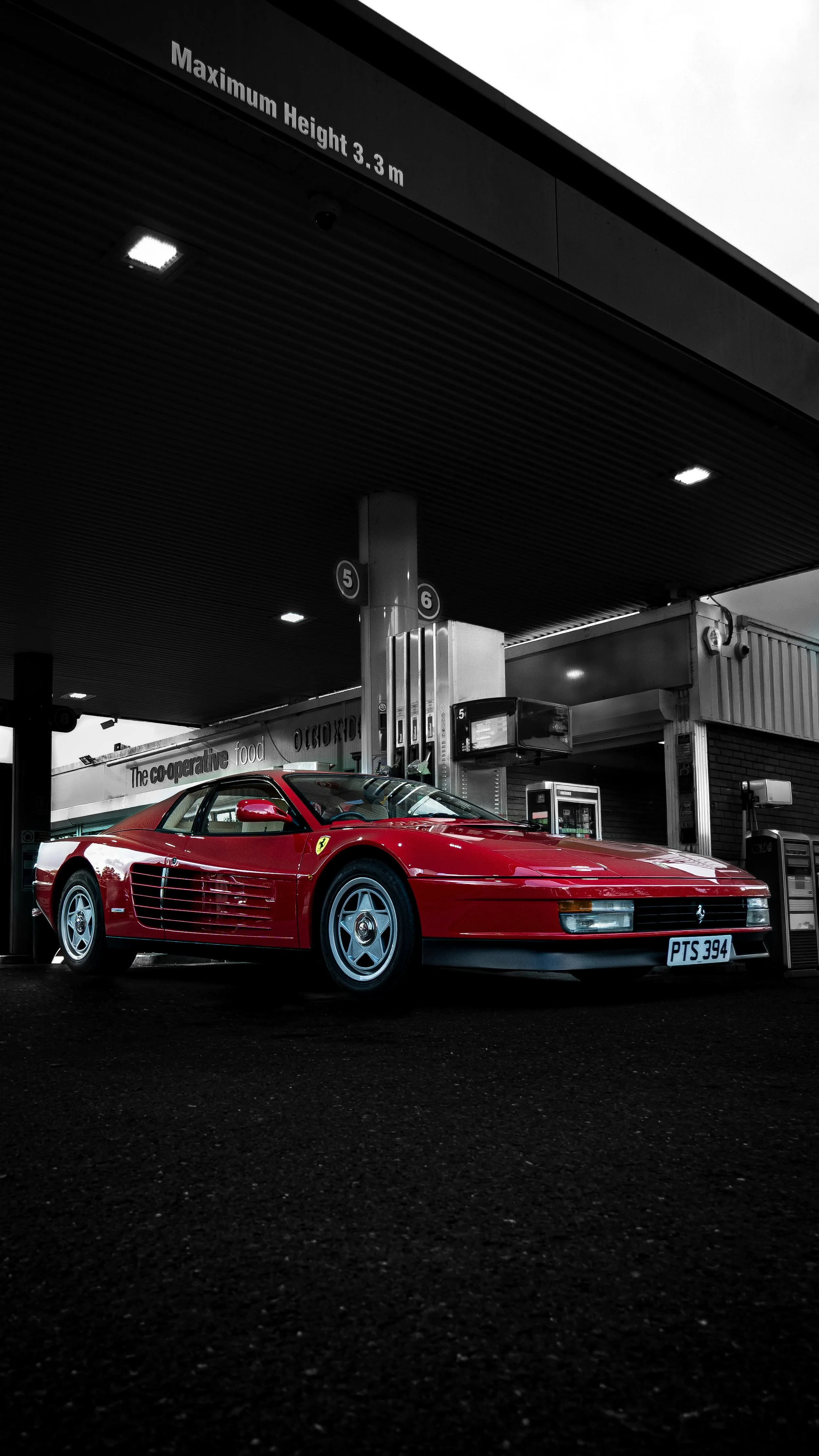 Red Ferrari sports car parked at a gas station under a canopy, with a maximum height sign indicating 3.3 meters.