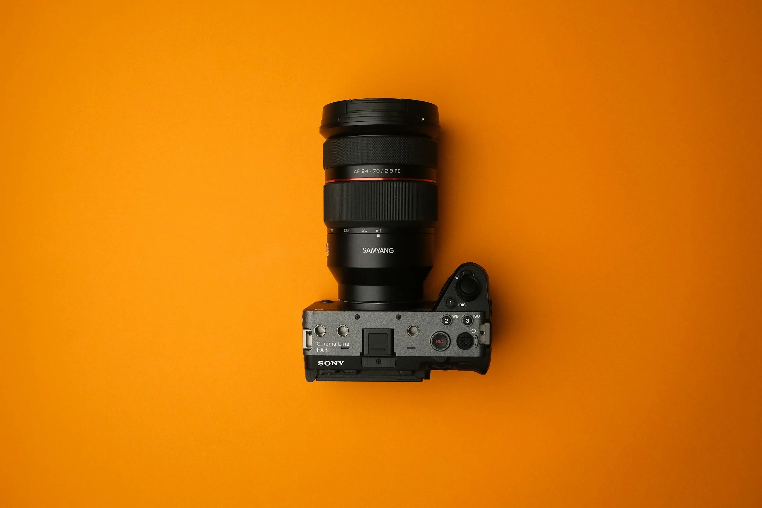 A Sony camera with a large Samyang lens attached, placed on an orange background.