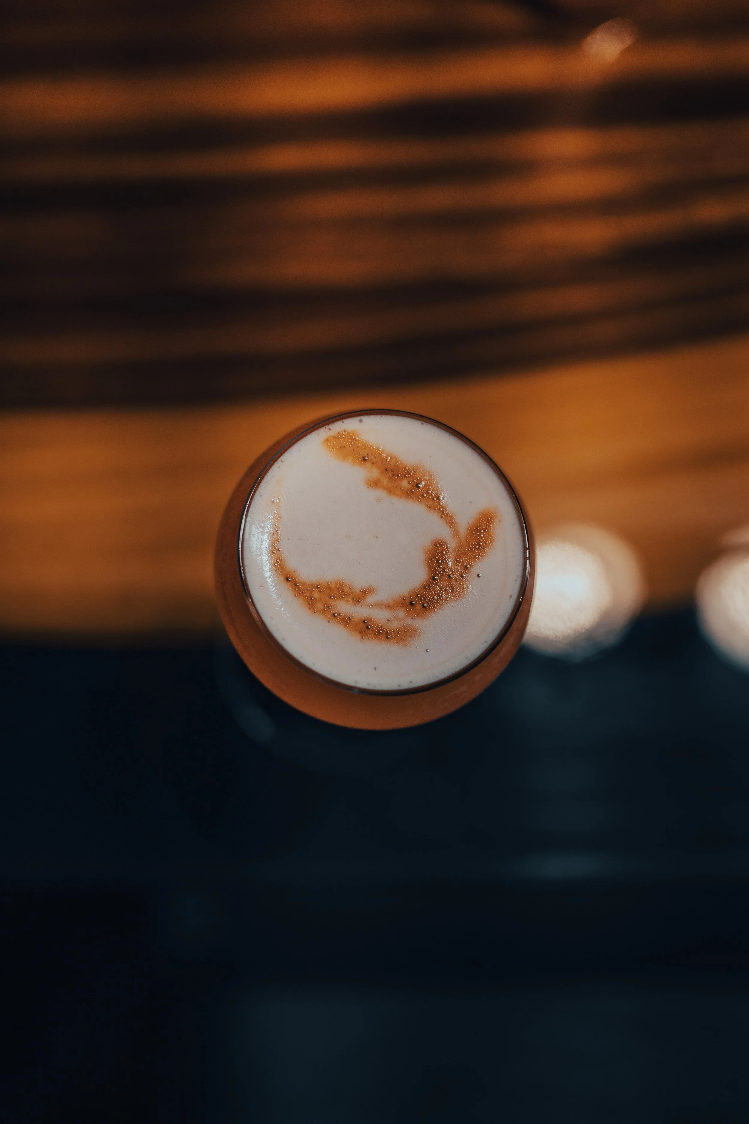 Top-down view of a glass of a brown beverage topped with foam and caramel drizzle, on a wooden surface.