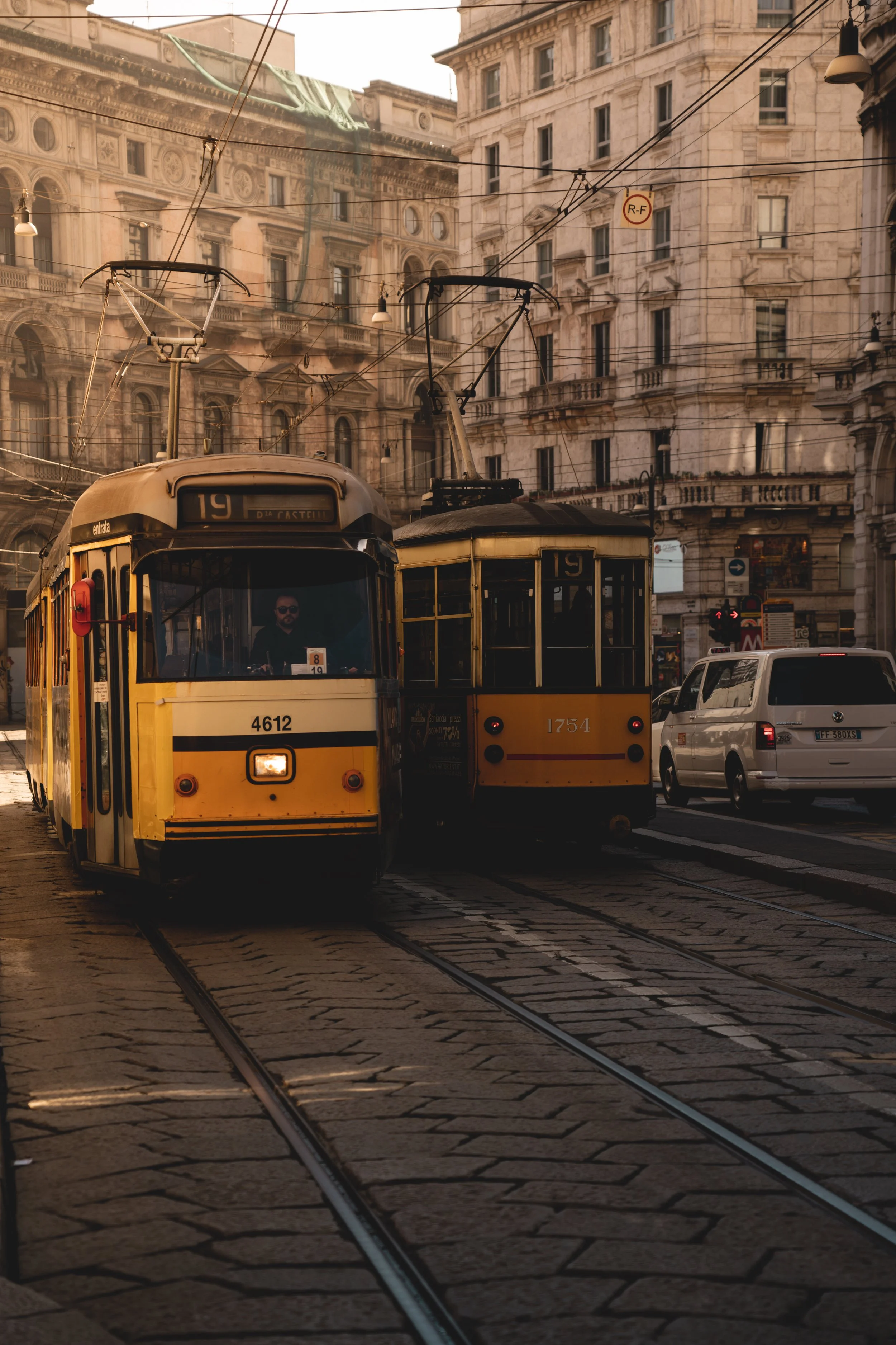Two yellow trams on a city street with old buildings in the background, during sunset.