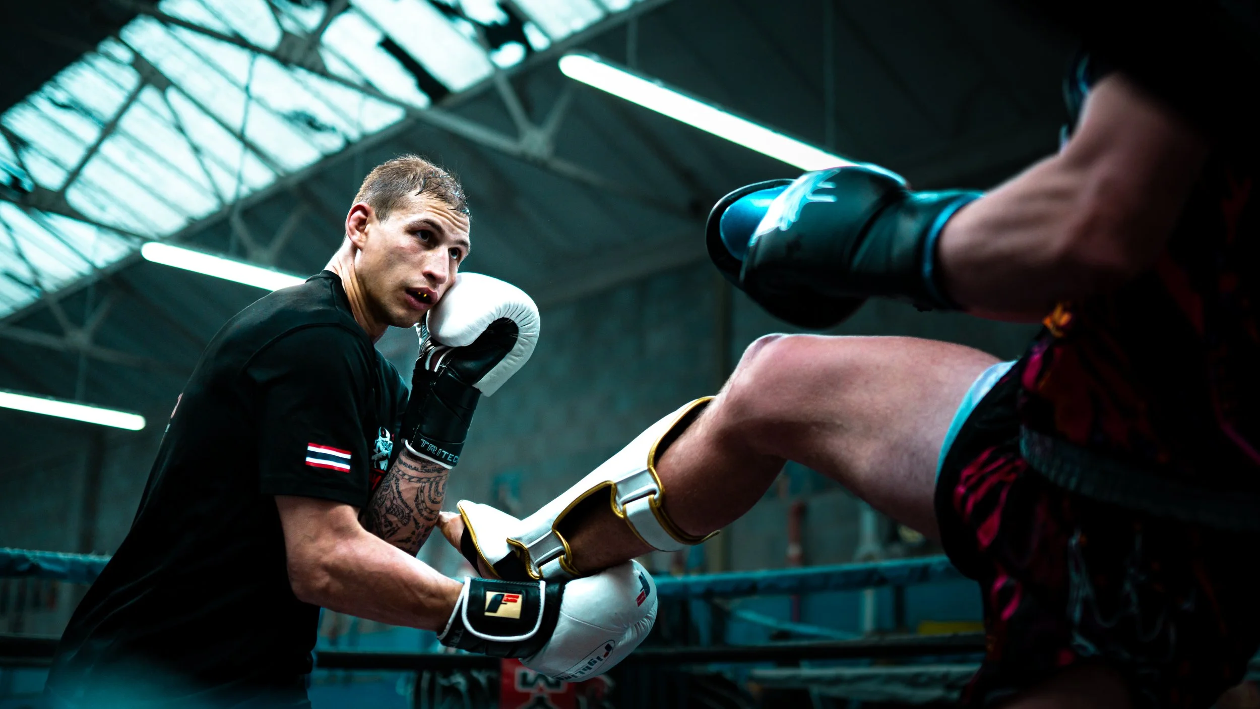 Two men boxing in a gym, one in black gloves preparing to punch the other in a intense sparring session.
