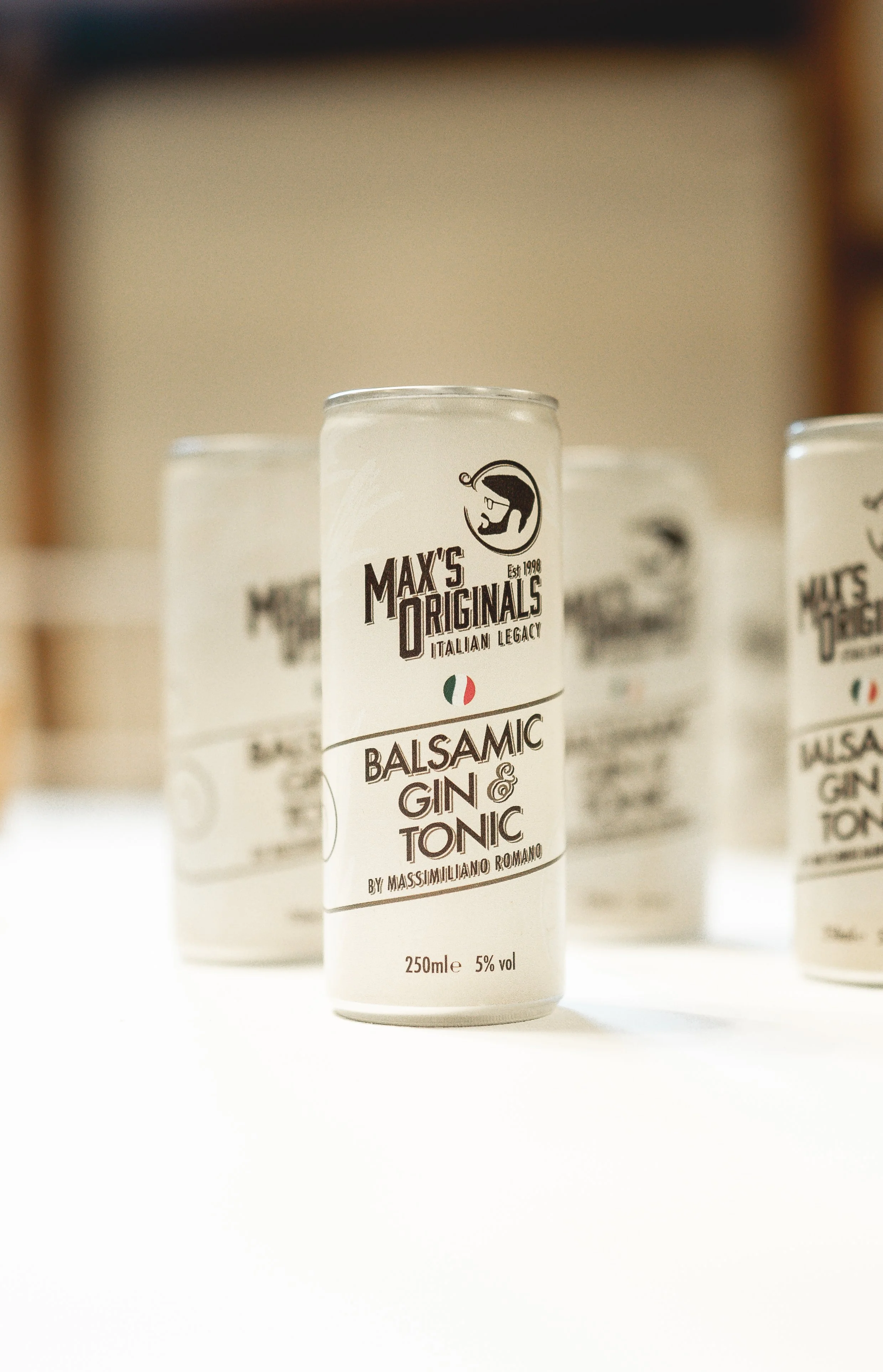 A can labeled Max's Originals Balsamic Gin & Tonic on a white surface with a blurred background.