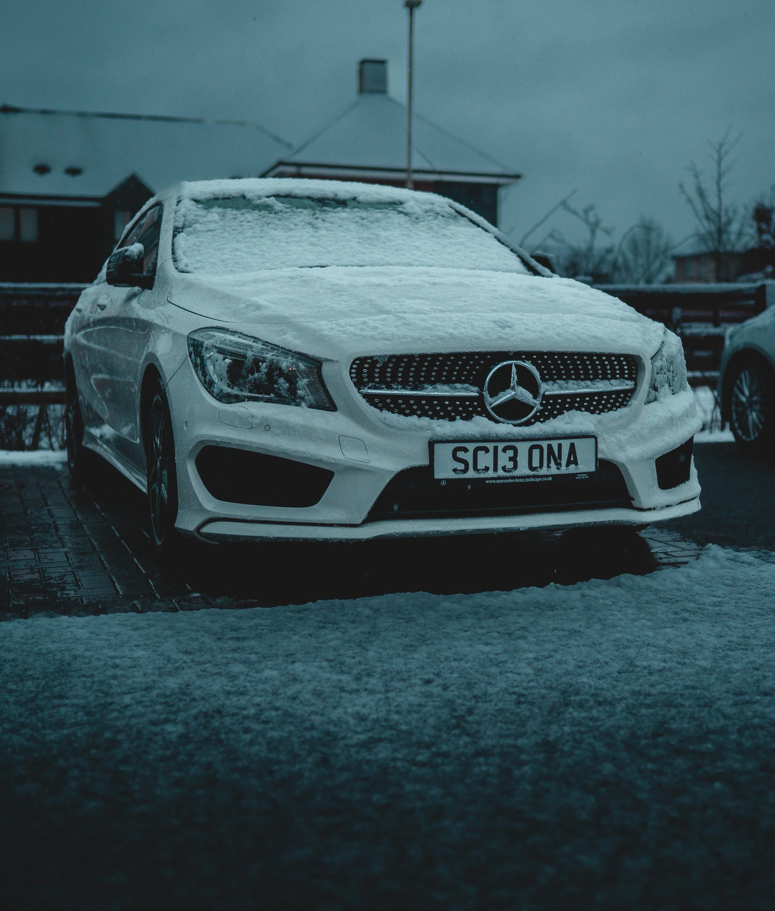 A white Mercedes-Benz car covered with snow parked on a driveway during winter.