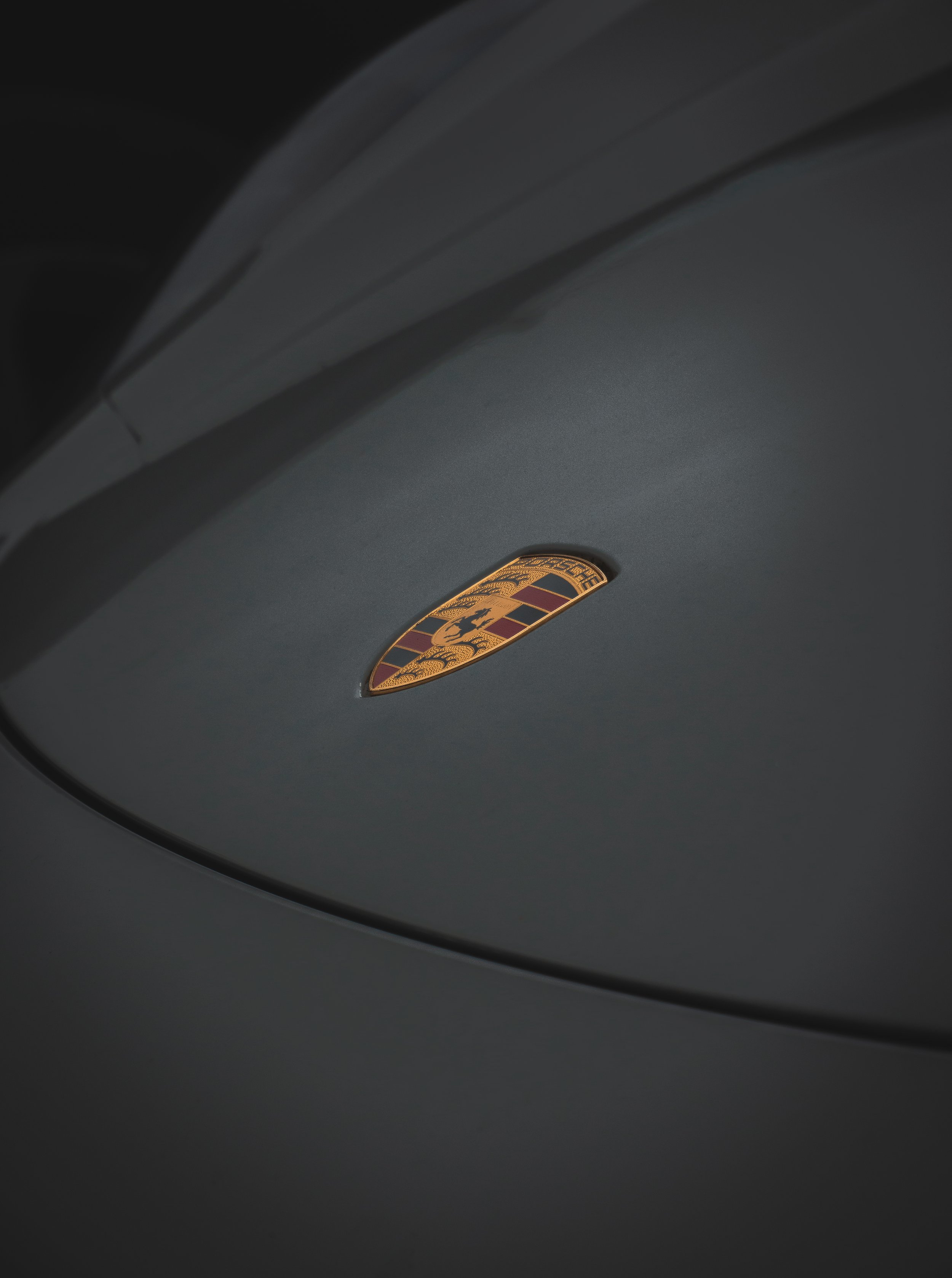 Close-up of a gray Porsche car with the Porsche emblem on the hood.