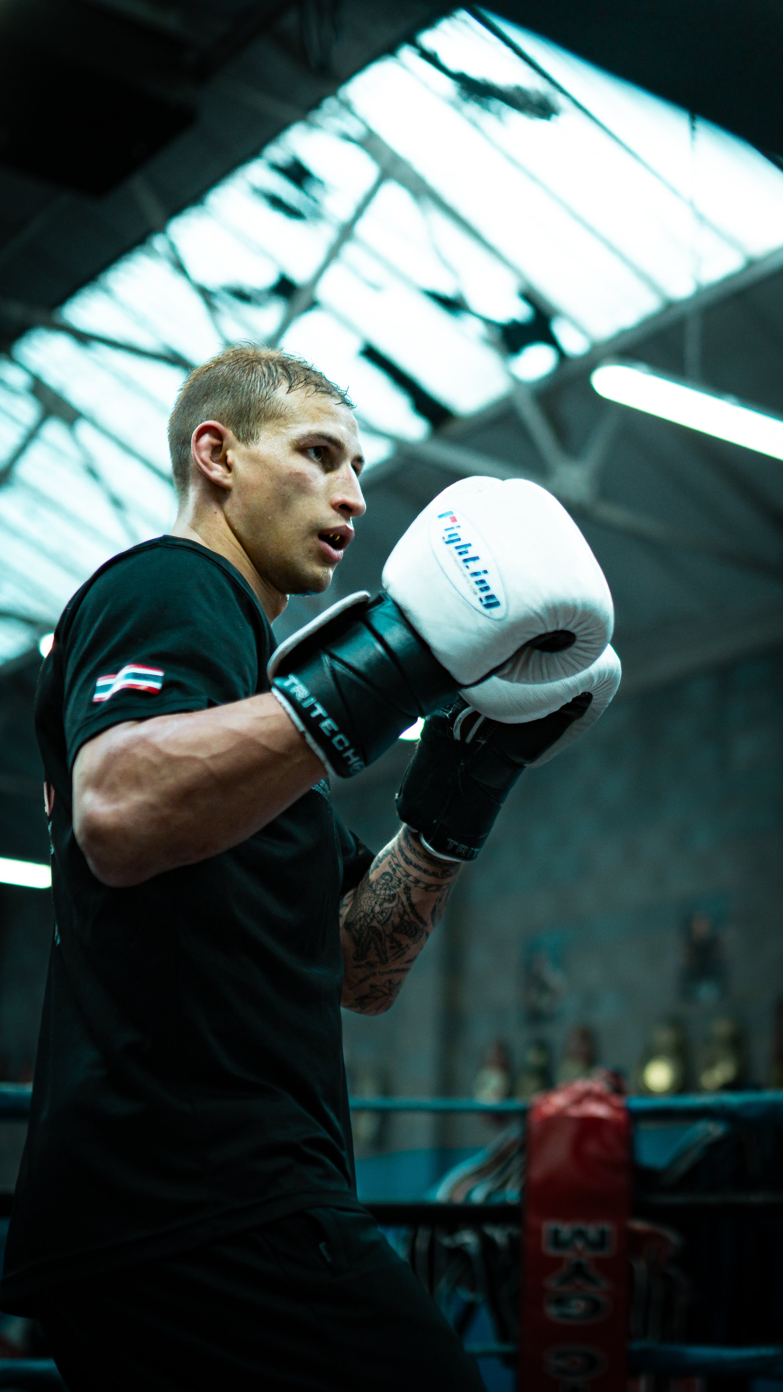 A male boxer wearing black training gear and white boxing gloves practicing in the gym.