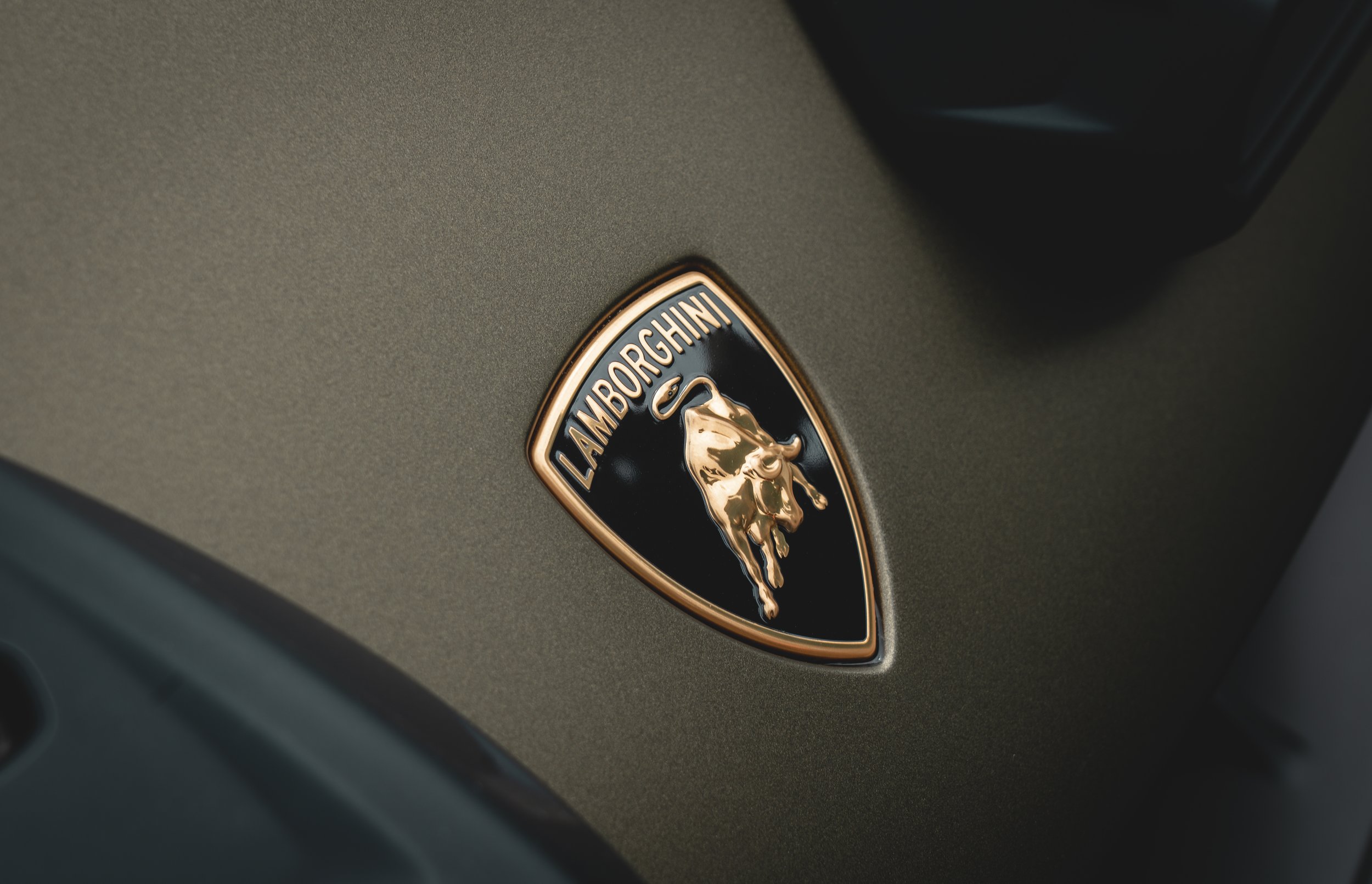 Close-up of a Lamborghini badge featuring a gold raging bull on a black shield background on a metallic surface.