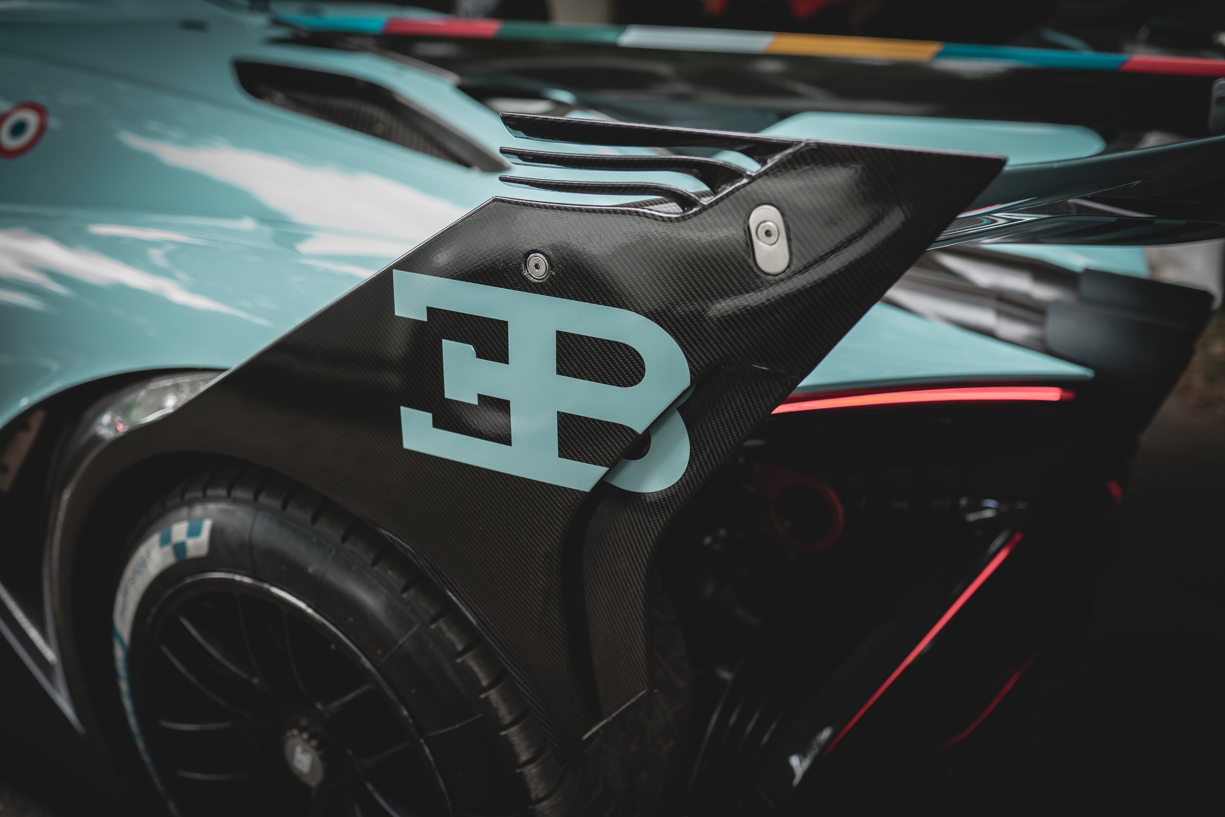 Close-up of a sports car with a black carbon fiber body part featuring a large blue letter 'B' and a blue square on it.