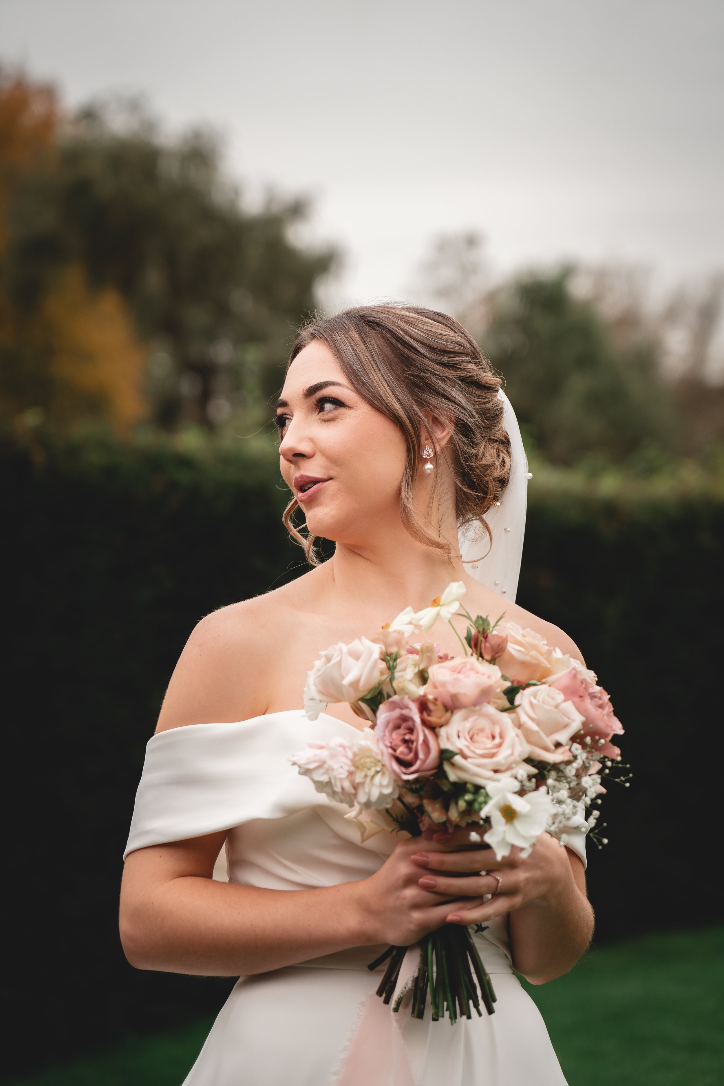 A bride holding a bouquet of pink and white roses outdoors on a cloudy day.