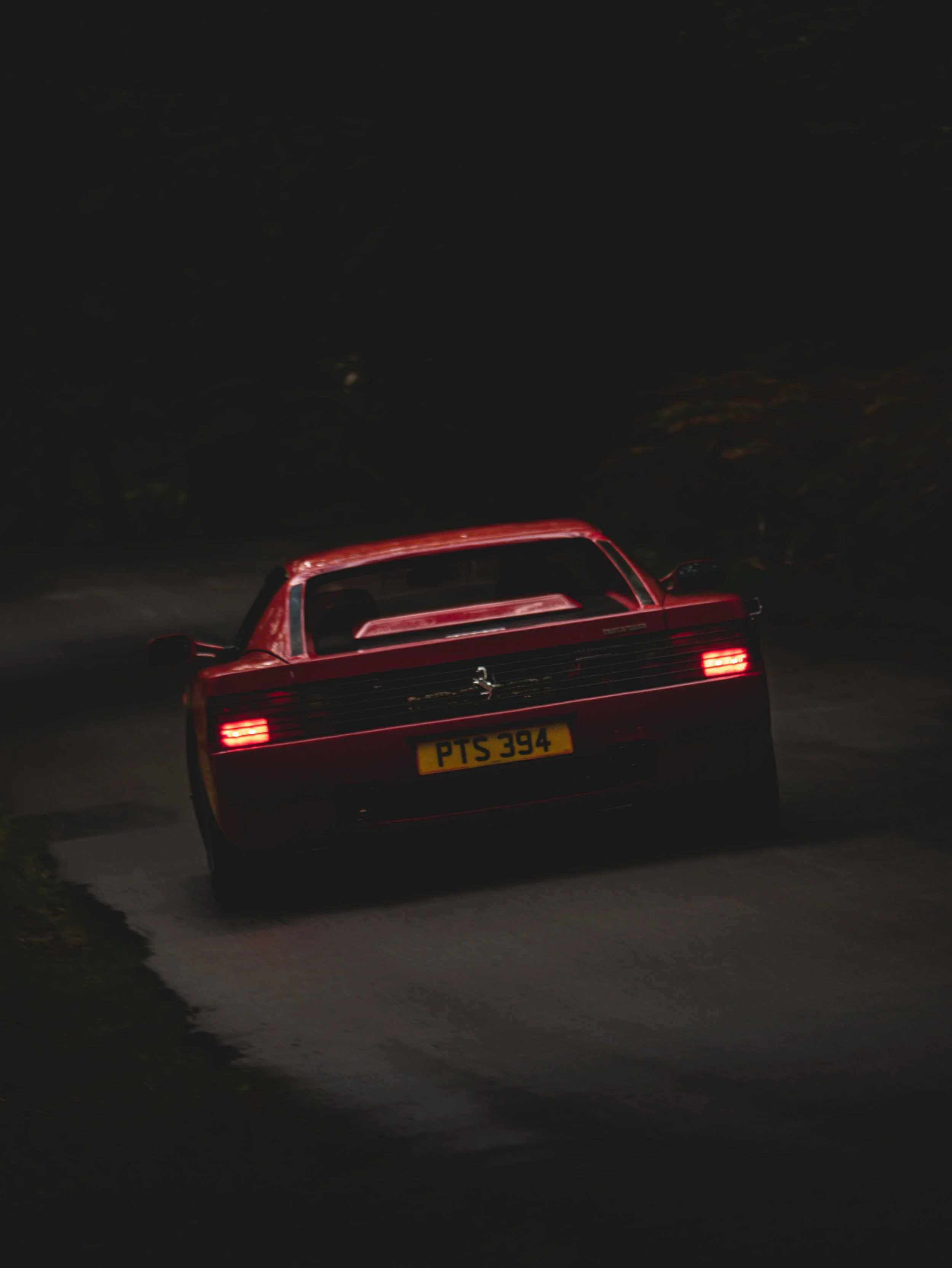 Red Ferrari car driving on a dark road at night with headlights on, view from the back