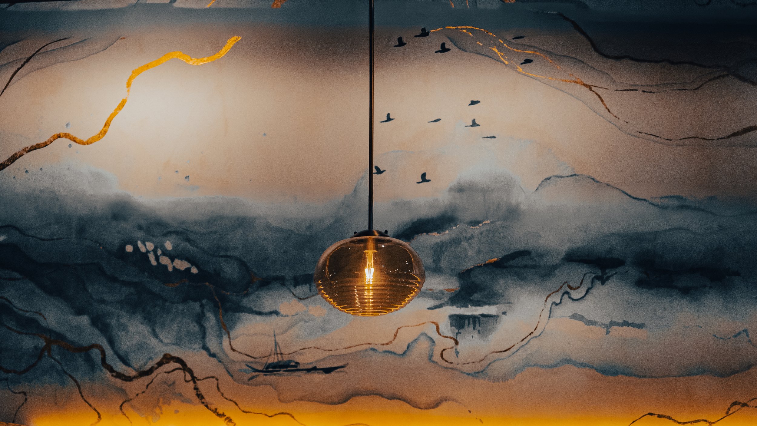 Ceiling mural depicting mountains, clouds, and flying birds, with a central hanging golden light fixture.