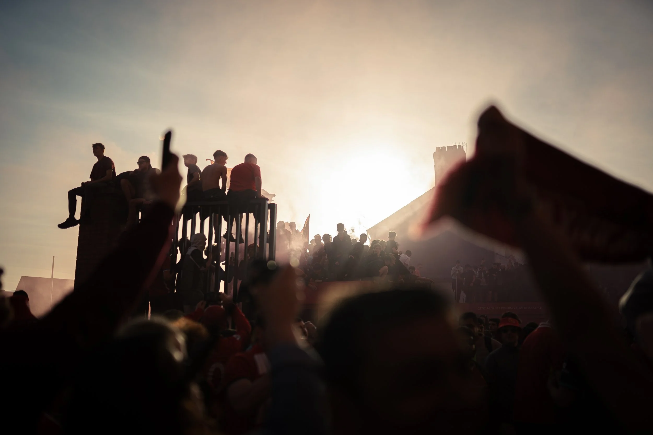 Crowd of people at a rally with some sitting on a raised platform and others standing below, during sunset.