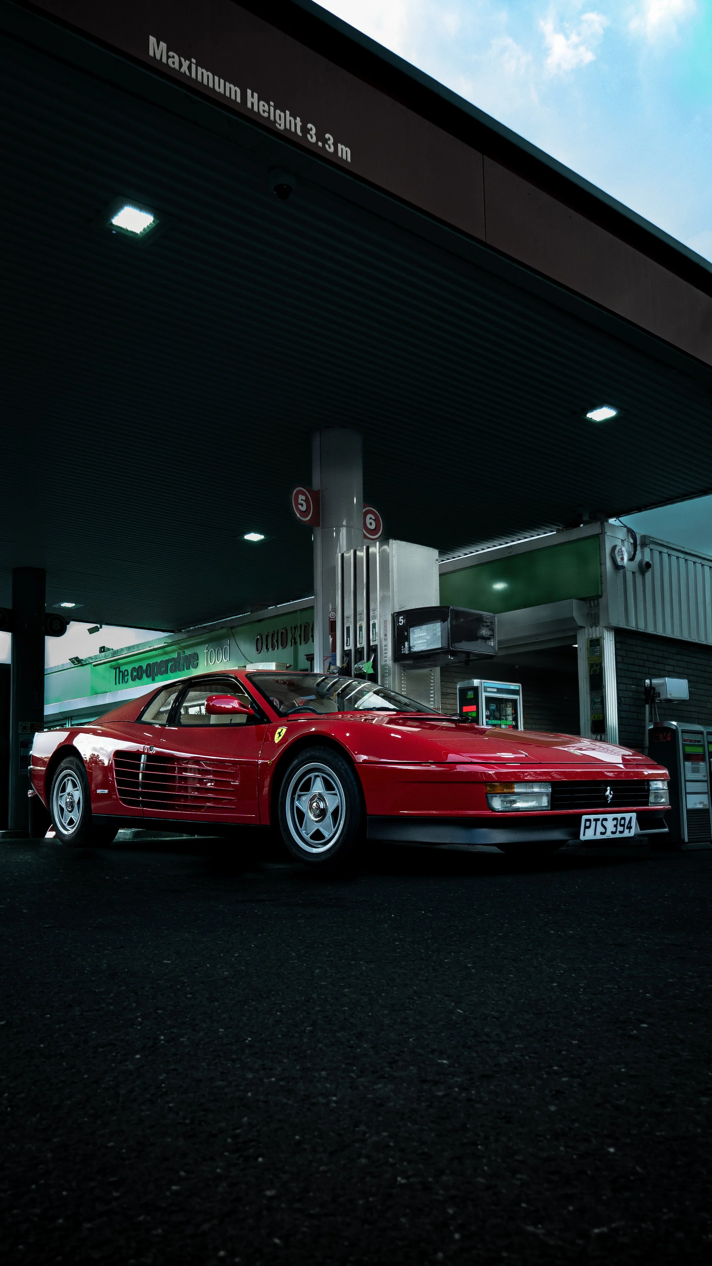 Red Ferrari sports car parked at a gas station pump with dark sky overhead
