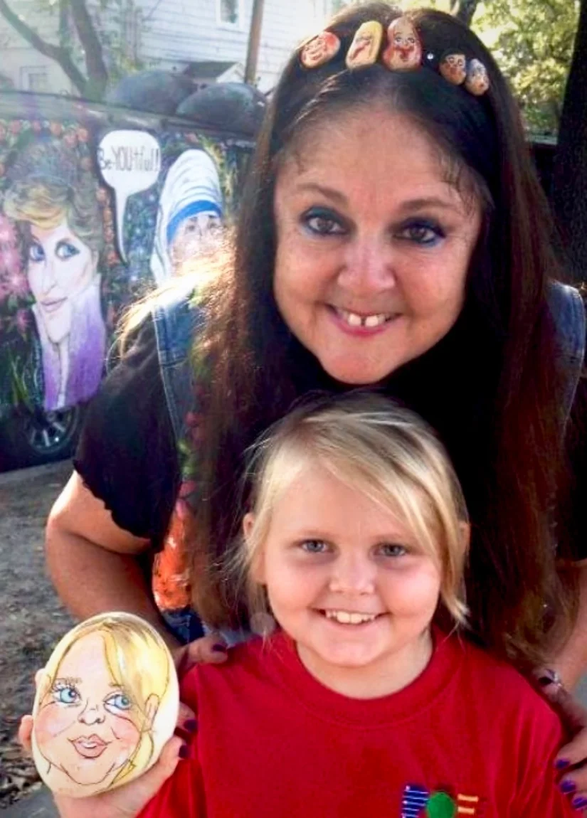 A woman and a girl smiling at the camera. In the background is an art car with paintings of Ellen DeGeneres and Mother Teresa on it.