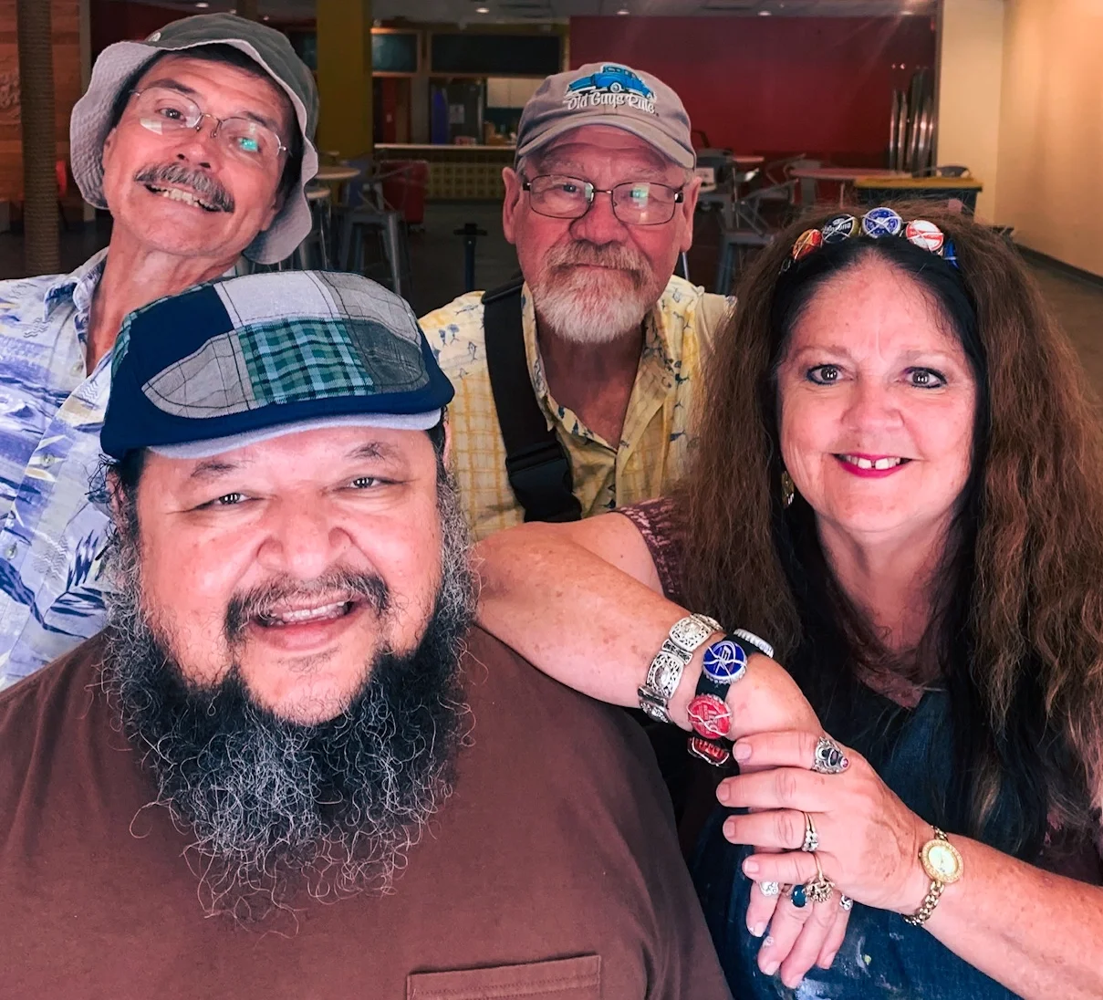 Five smiling adults, two men and three women, posing closely together indoors, with colorful background.