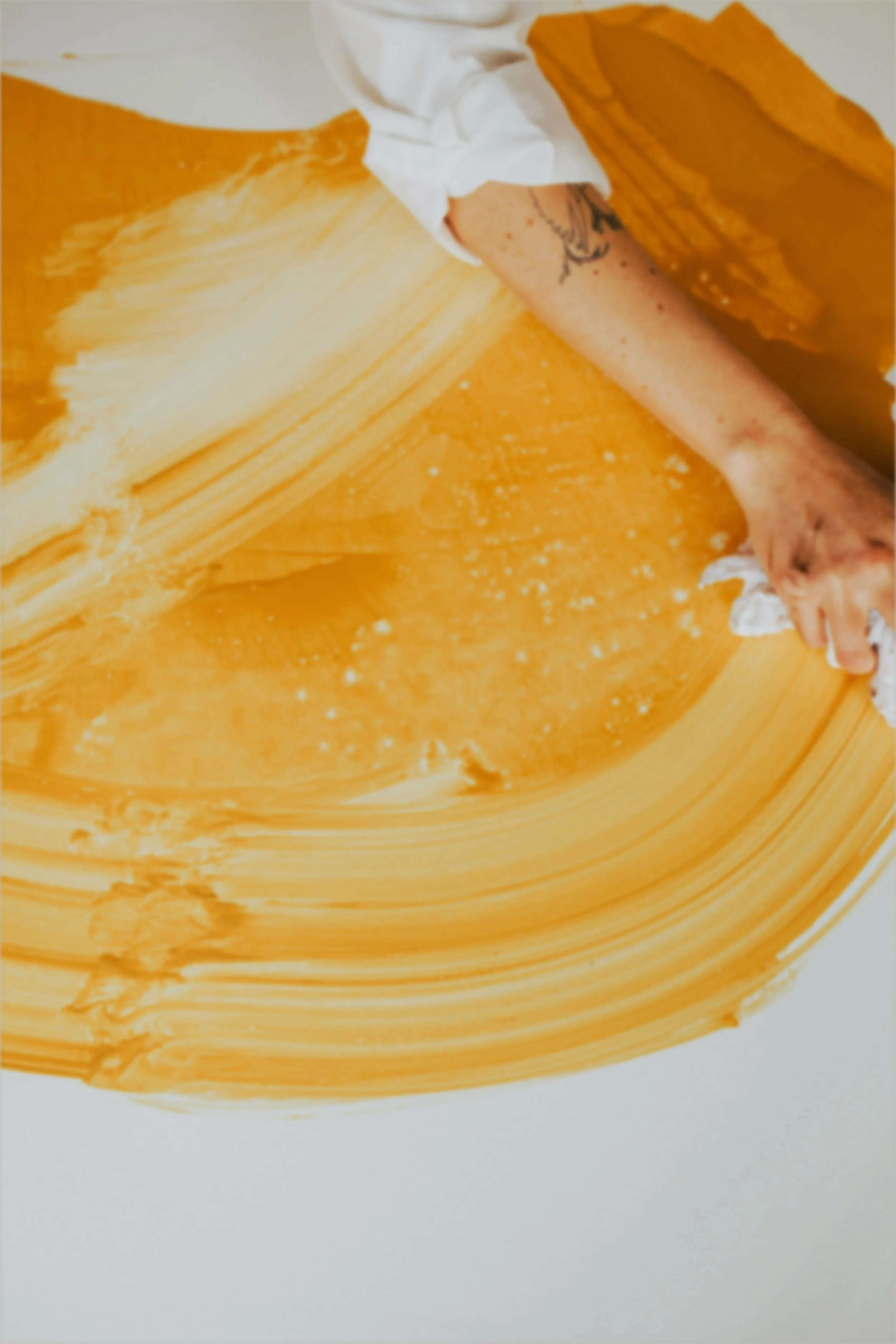 A woman smearing yellow paint across a white surface in a circular arc.