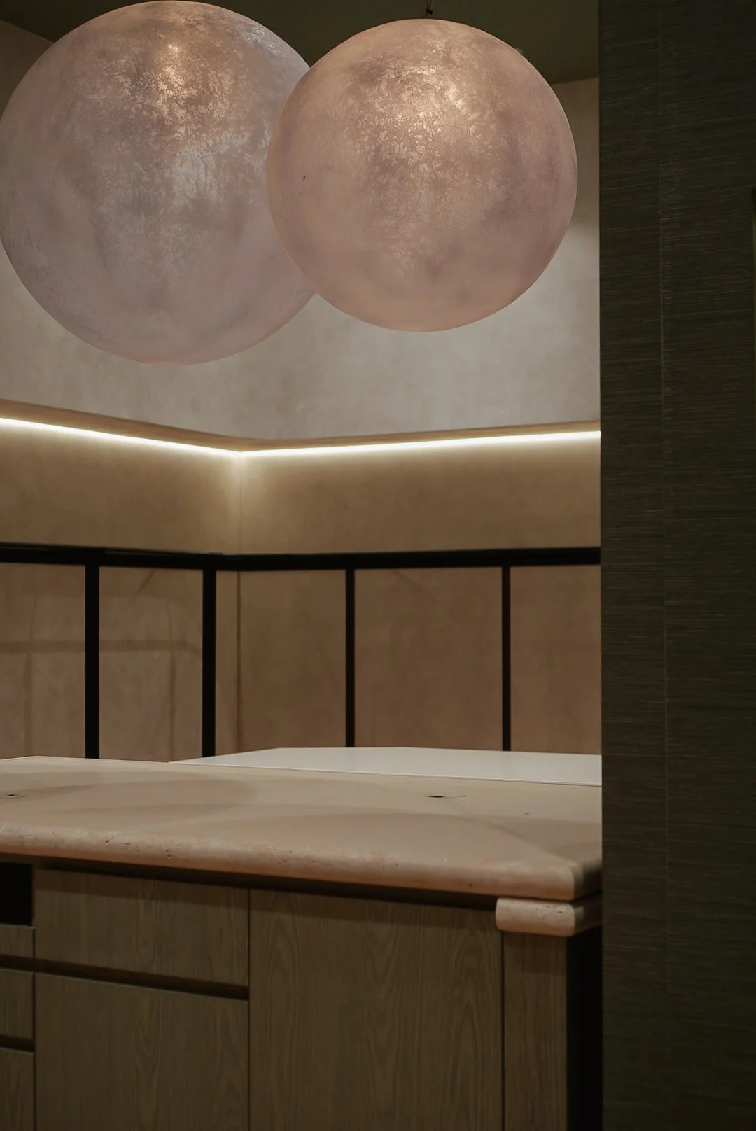 Two spherical ceiling lights in a modern interior space, positioned above a marble countertop with a wooden cabinet below and a black metal railing.