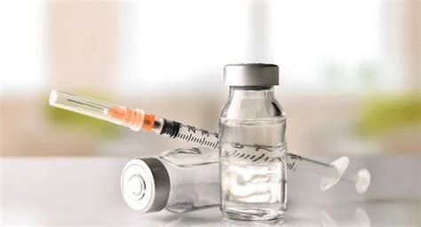 Two vaccine vials and syringes on a white surface.