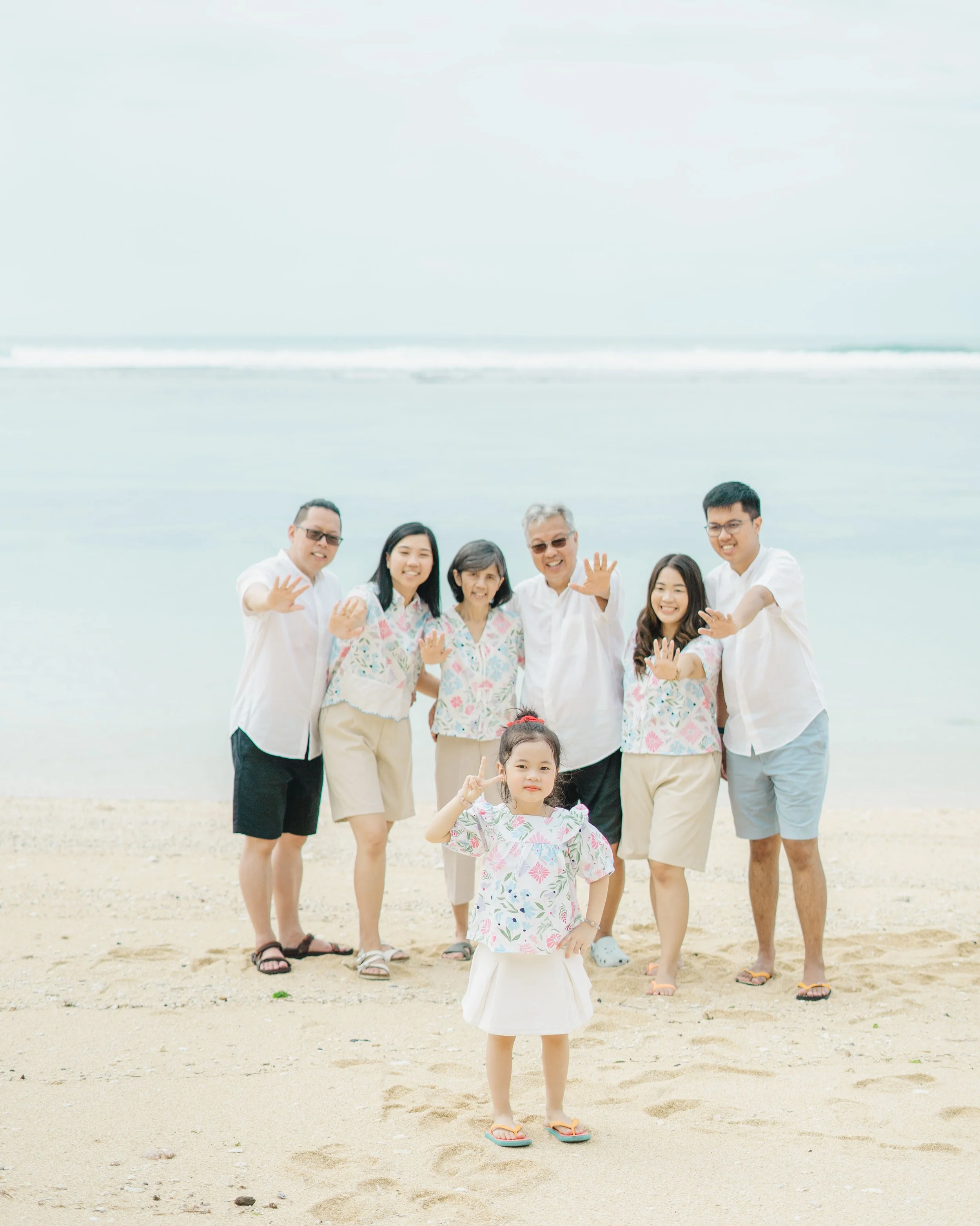 Family standing on a beach with the ocean in the background, waving at the camera.