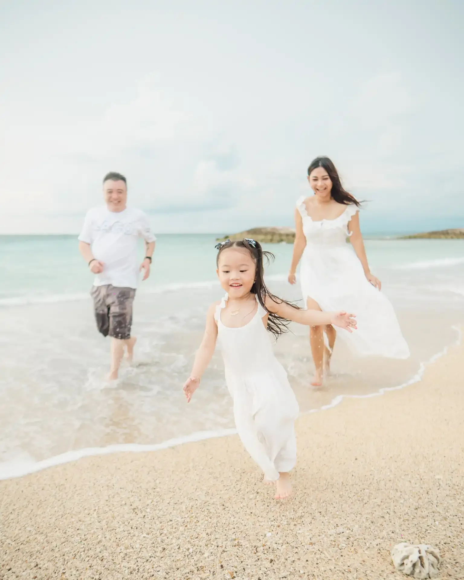 A family of three children running on the beach near the ocean, laughing and enjoying the water.