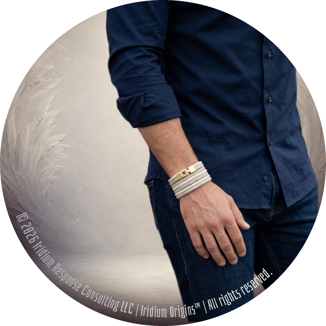 Partial view of a man wearing a navy blue shirt and jeans, with his left hand resting near his pocket and a layered beige bracelet on his wrist, against a background with a decorative feather motif.