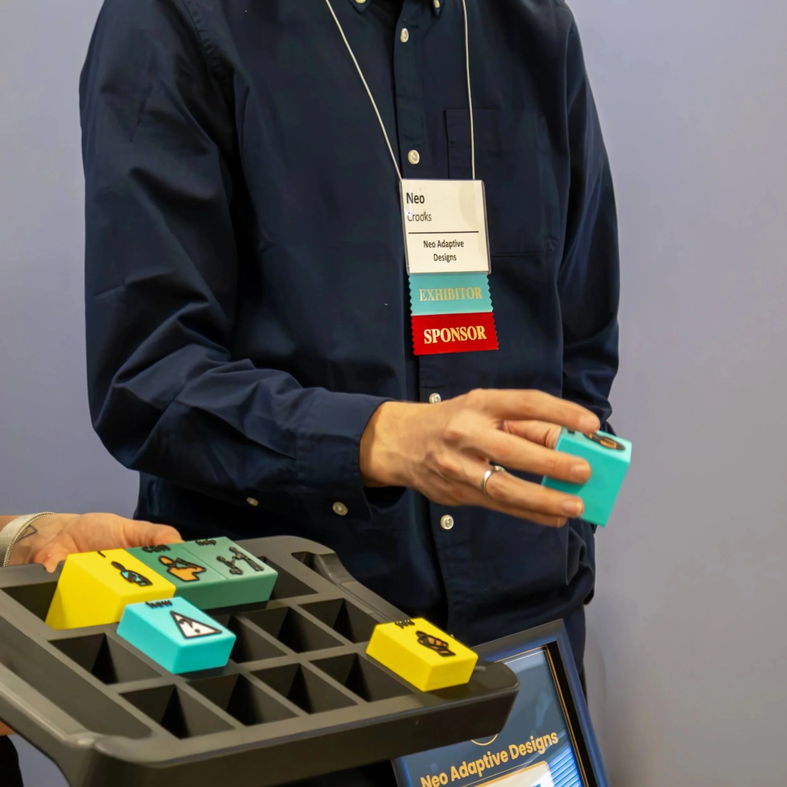 Neo Crooks, founder of Neo-Adaptive Designs, holding Tactile Voices tactile AAC blocks at the CSHA 2026 booth