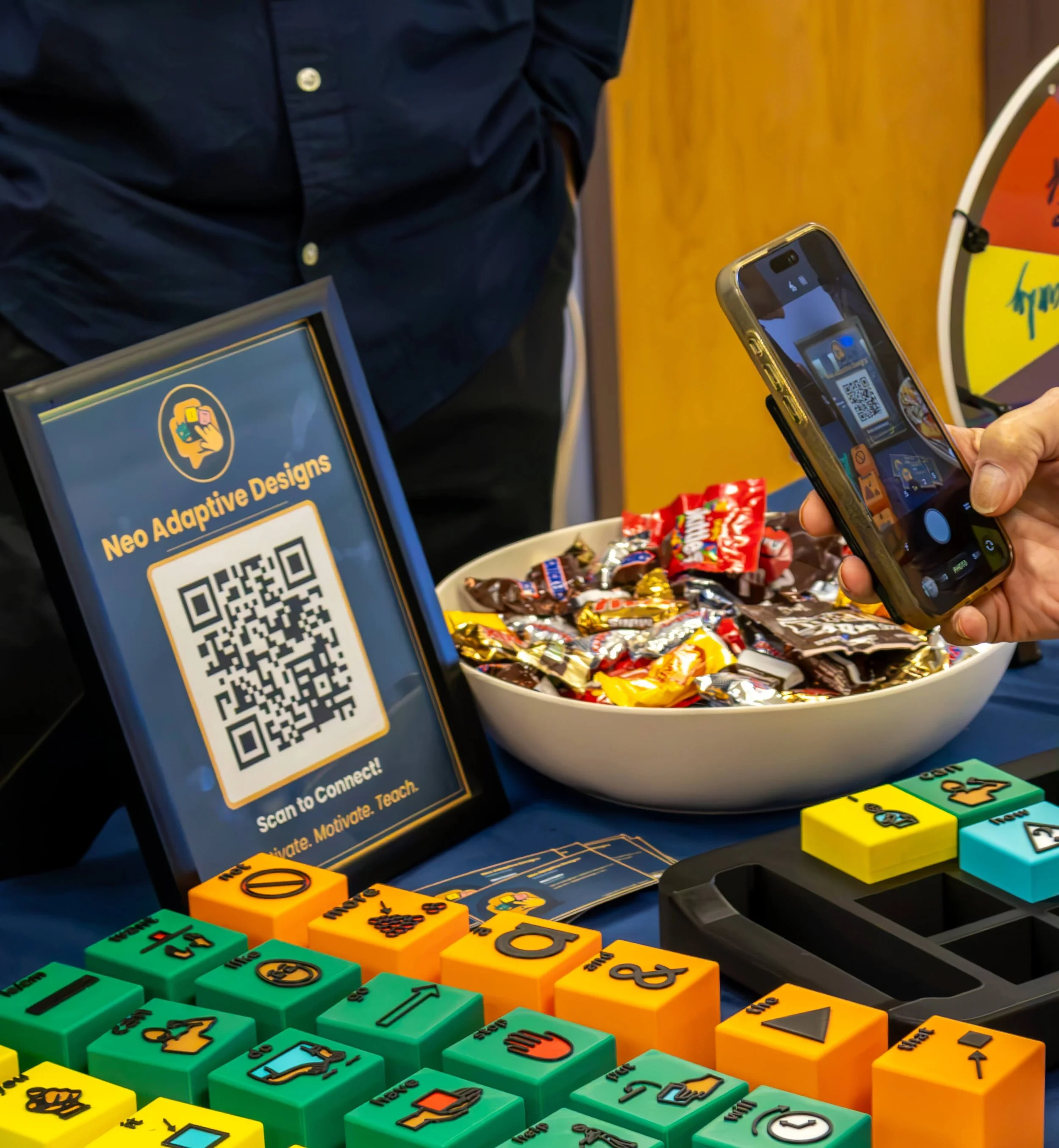 Visitor scanning a QR code at the Tactile Voices booth next to colorful tactile AAC blocks at CSHA 2026