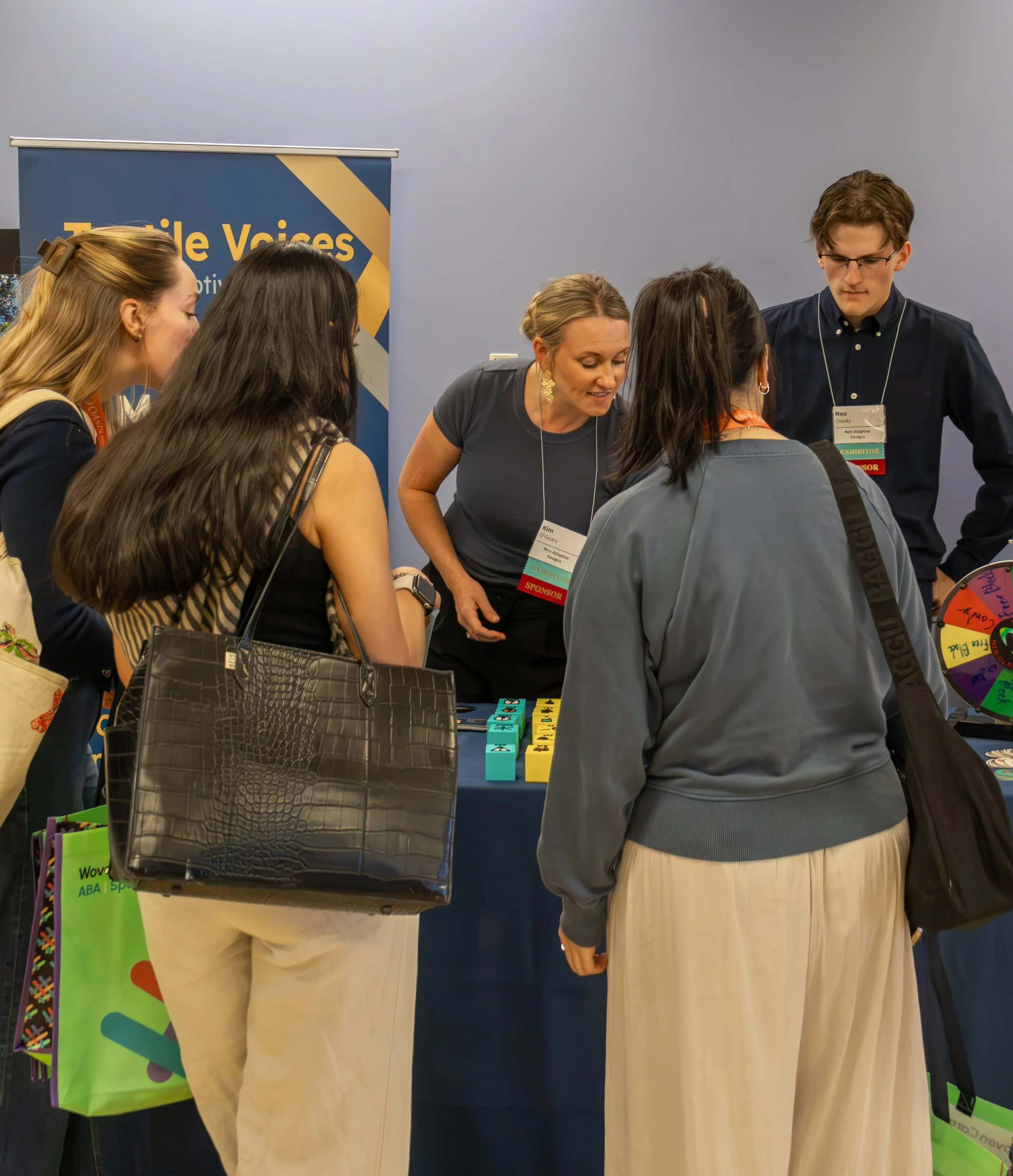 Conference attendees talking at the Tactile Voices booth at CSHA 2026, with tactile AAC blocks and a prize wheel on display