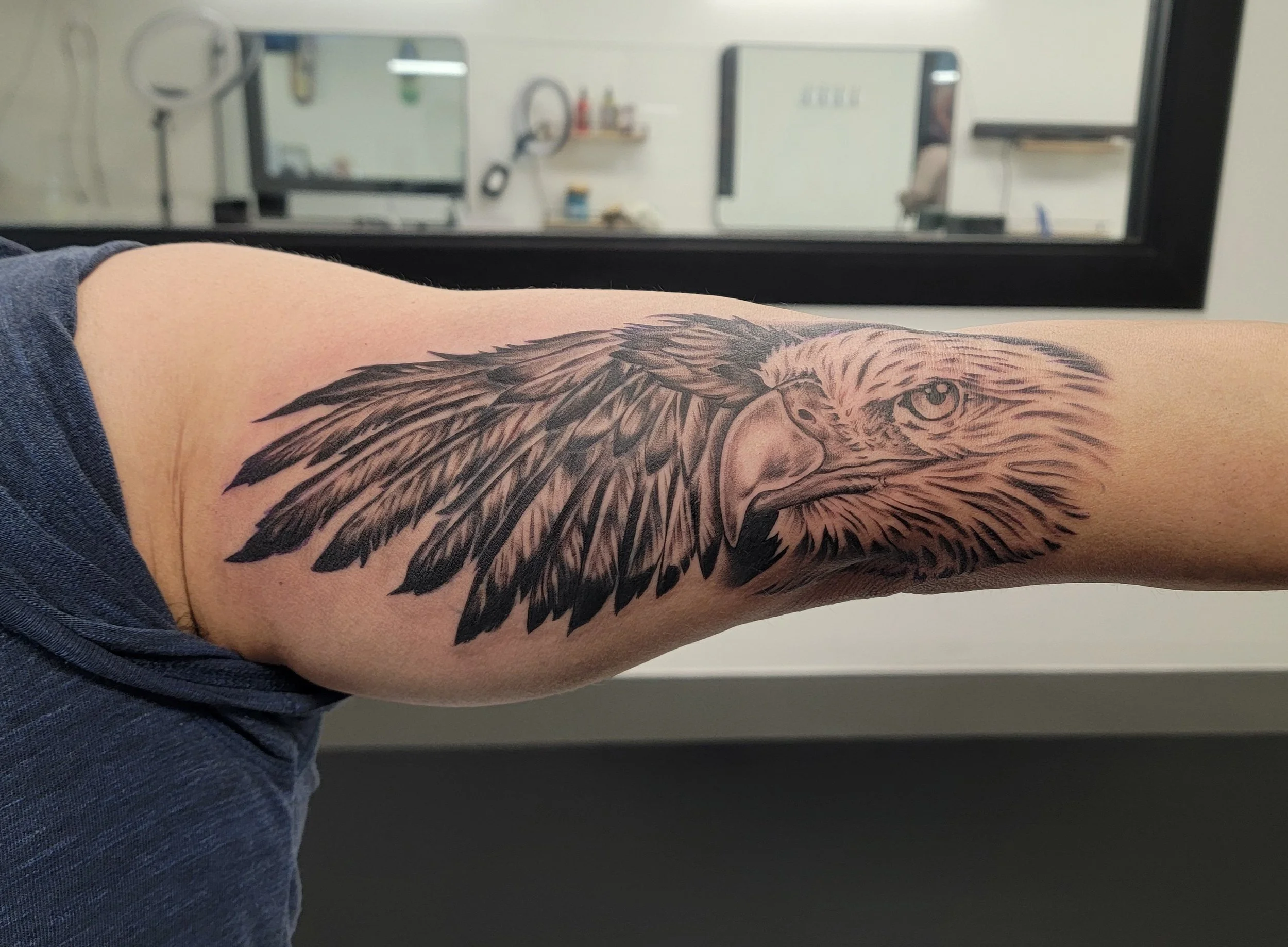 Tattoo of an eagle's head with detailed feathers on forearm