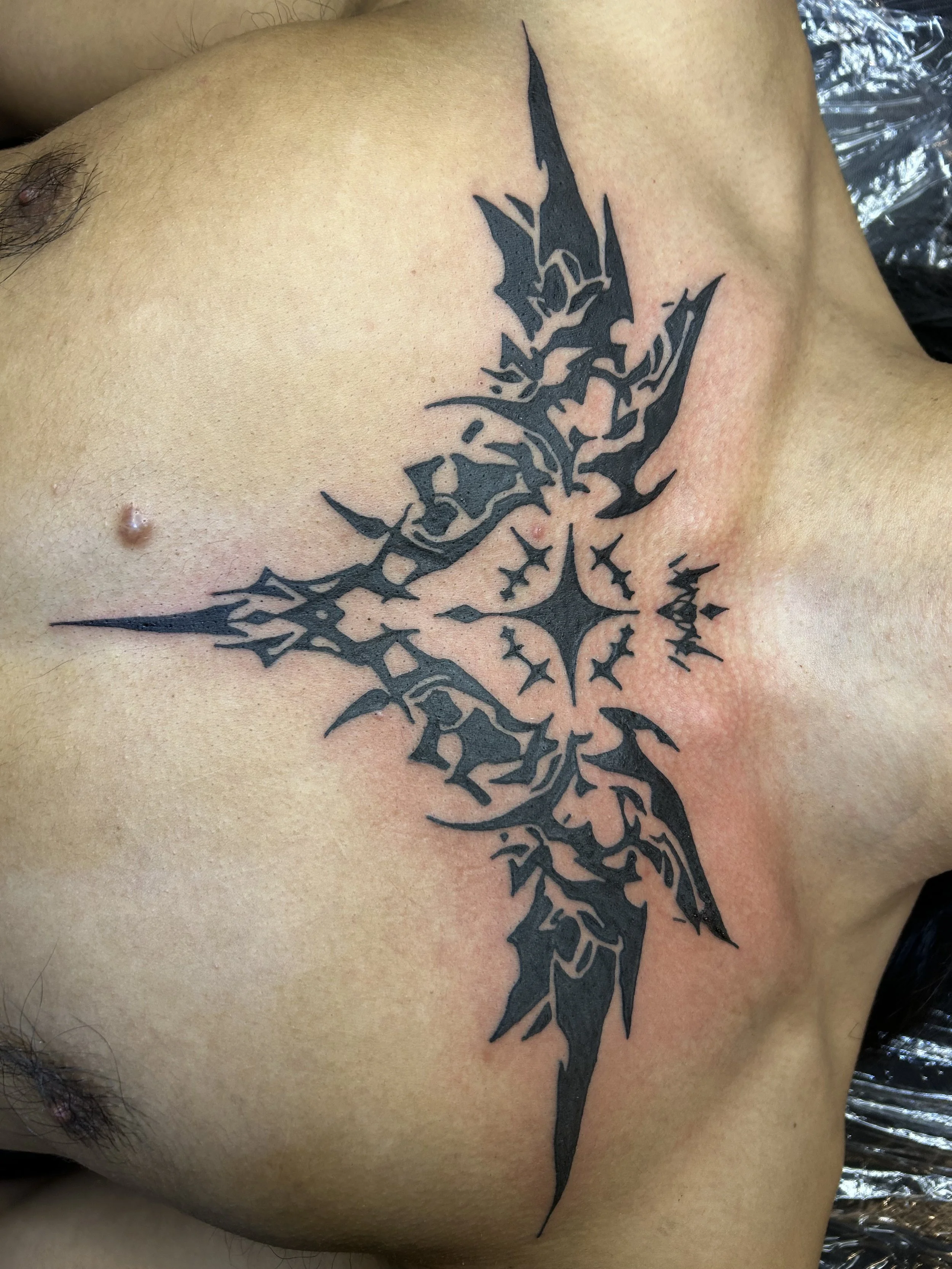 A black tribal-style tattoo of a dragon on a person's upper chest.