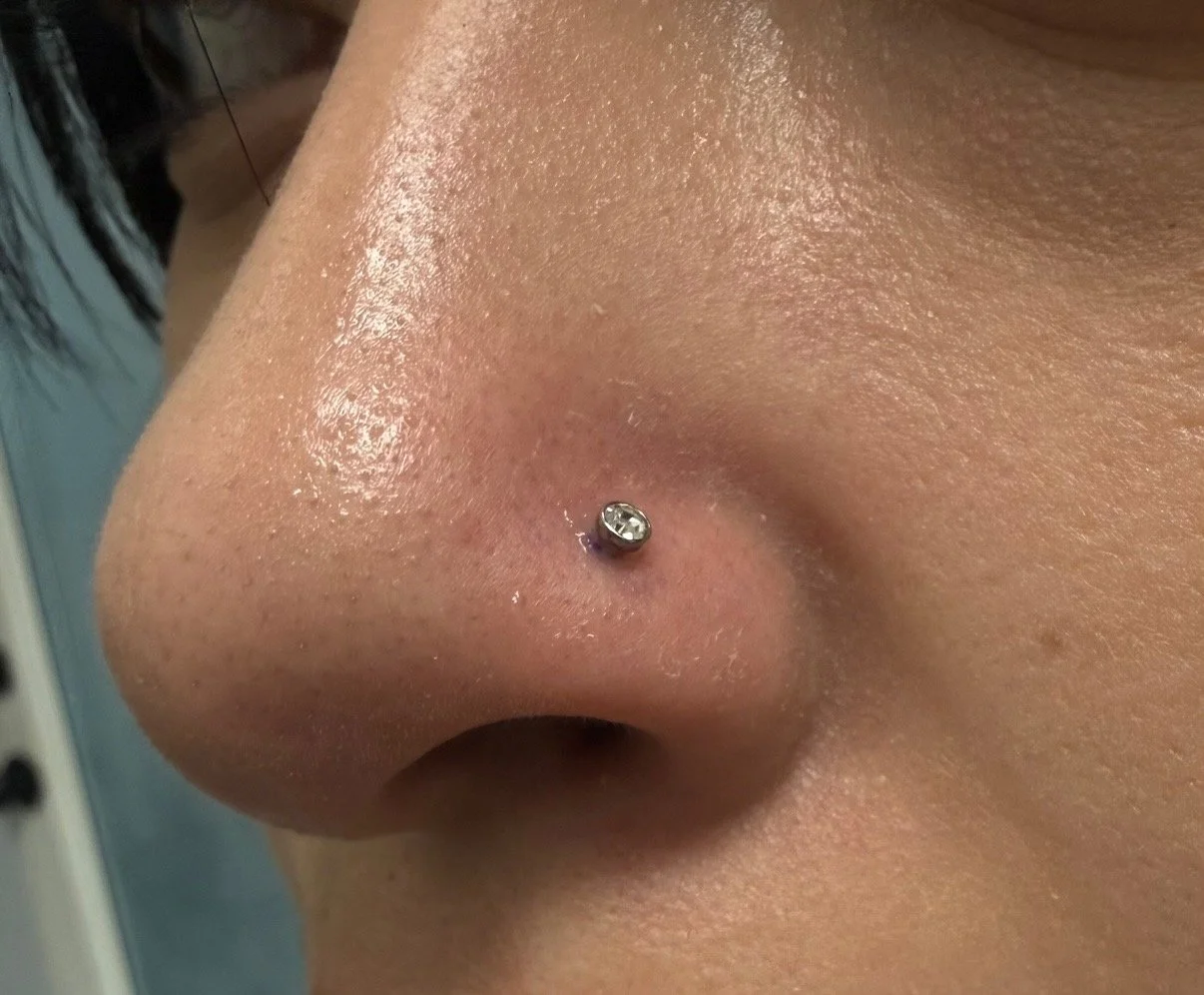 Close-up of a person's nose with a small, clear gemstone nose stud piercing.