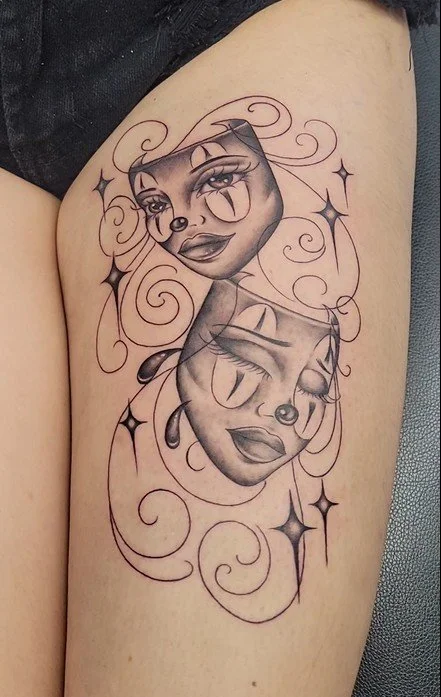 Tattoo of two stylized female clown faces surrounded by swirling lines and star-shaped accents on upper arm.