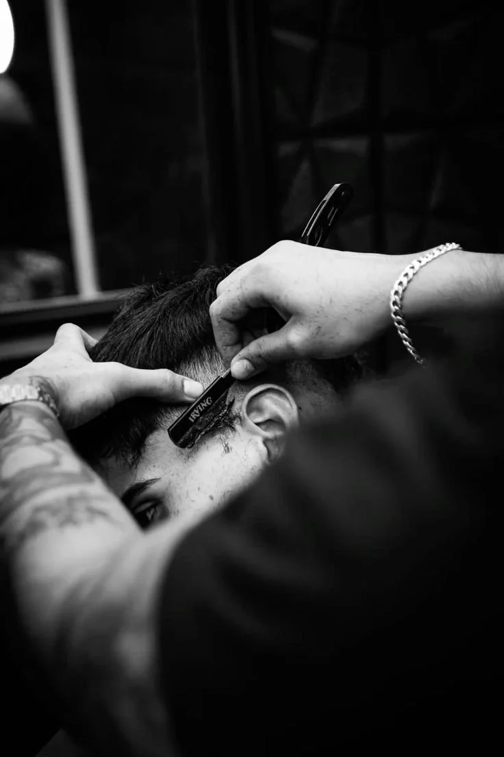 A person with short hair getting a haircut in a barbershop, viewed from a close angle in black and white.