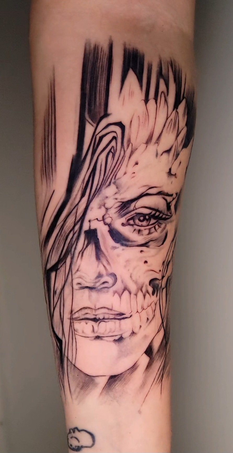 Black and gray tattoo of a woman's face with detailed eye, nose, lips, and skull elements.