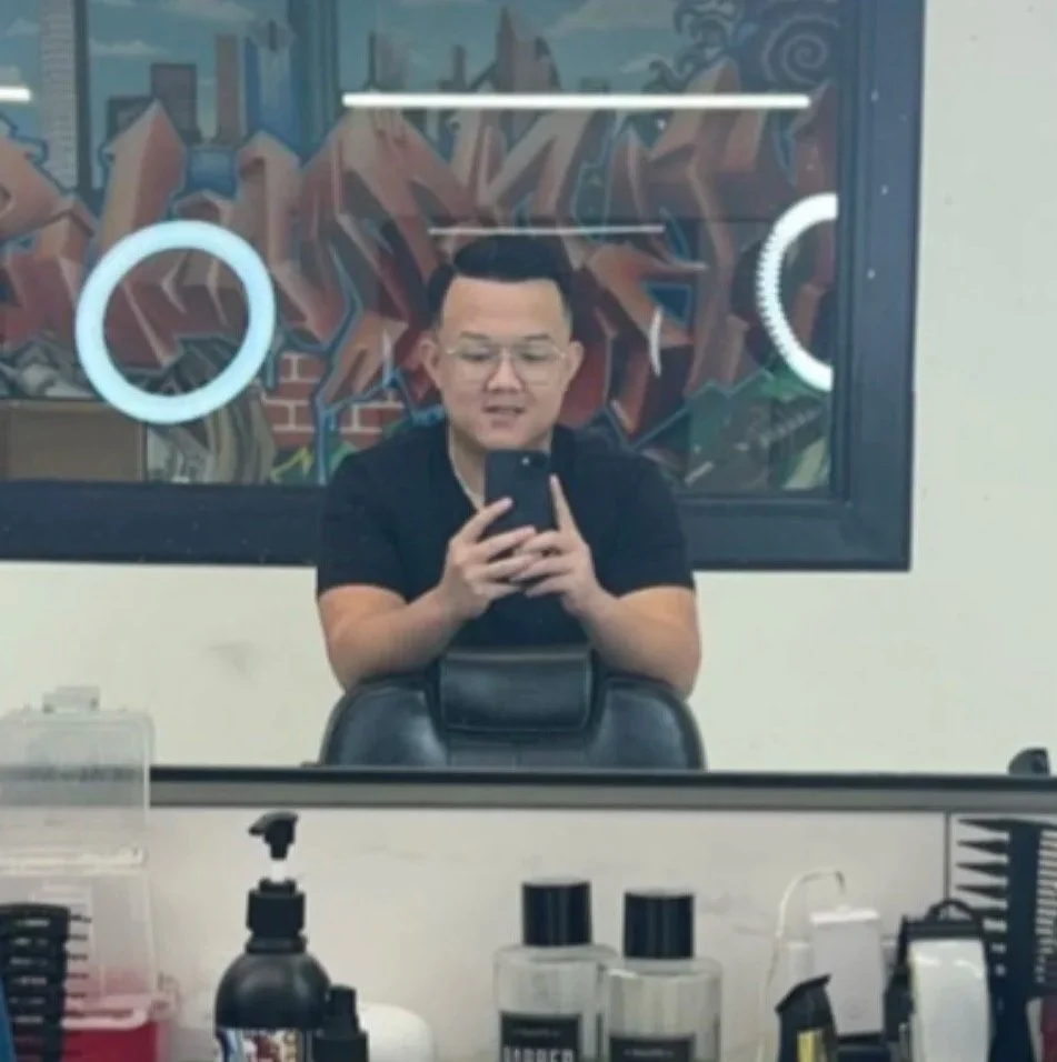 A young man taking a selfie in a salon mirror, with a graffiti-style mural on the wall behind him.