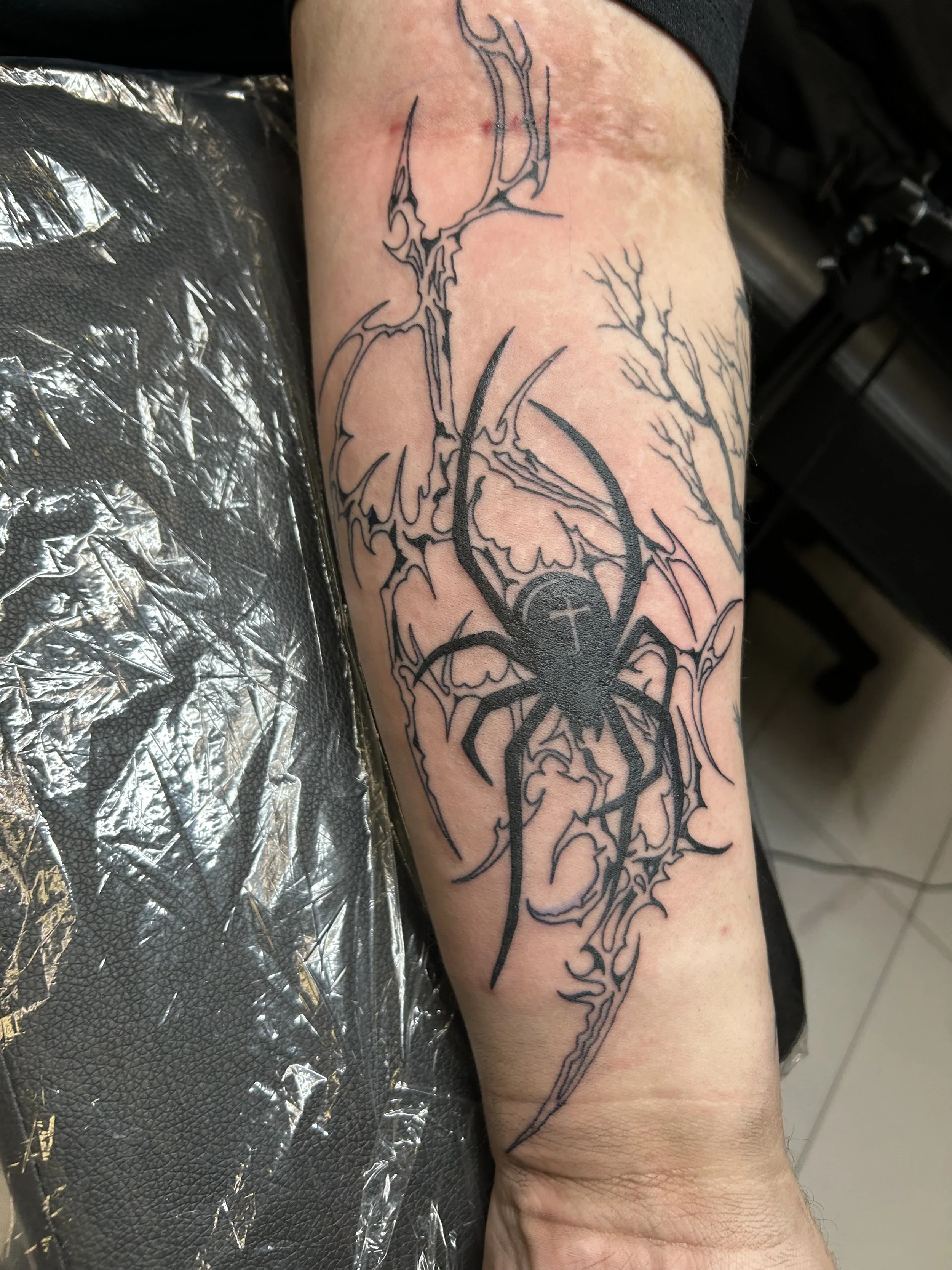 Tattoo of a spider with elongated legs on a person's forearm, with jagged, abstract lines and designs surrounding it.